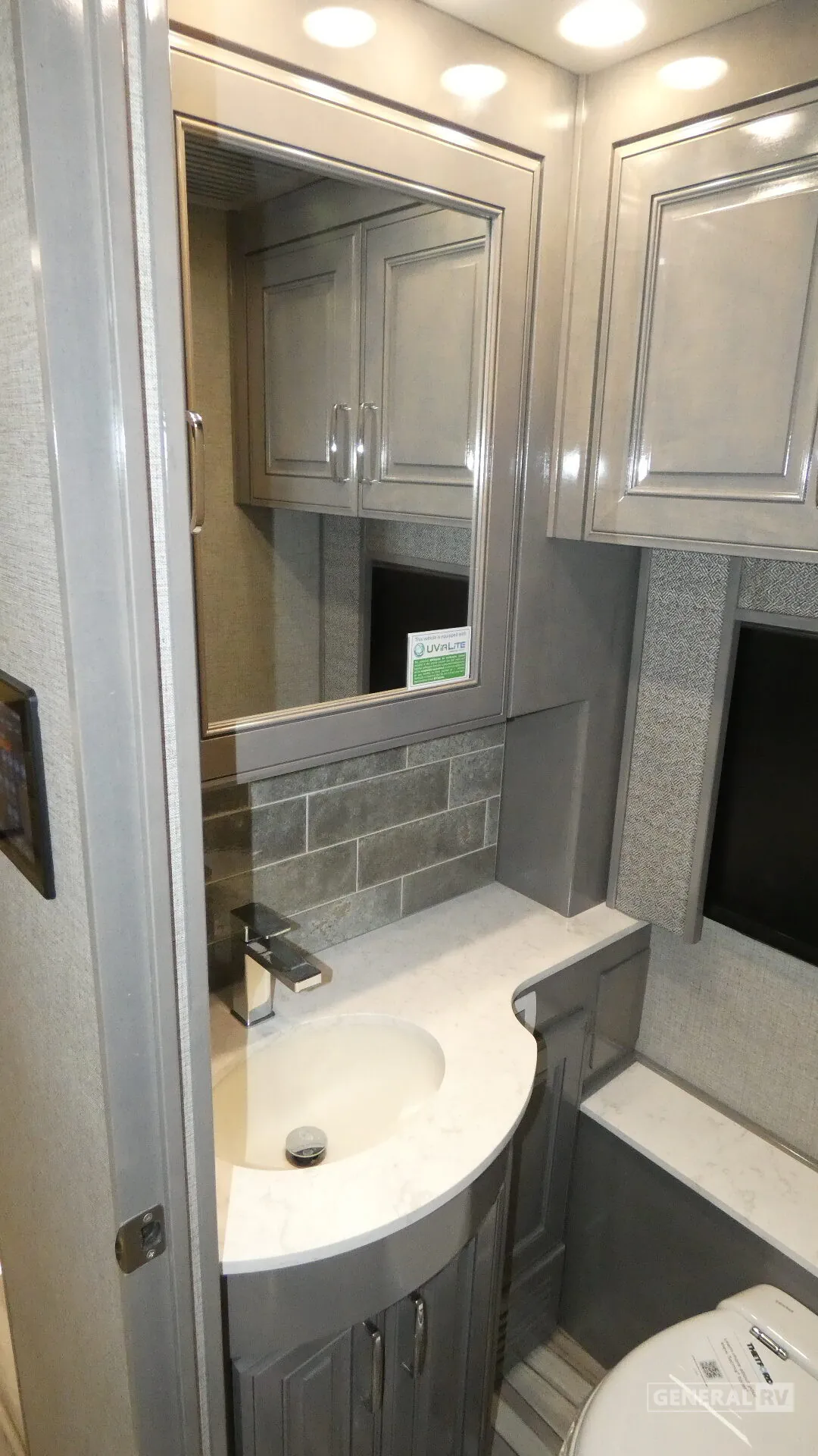 2026 American Coach American Dream 45A — Motorhome bathroom vanity with curved sink, faucet, mirrored cabinet, toilet, and surrounding storage