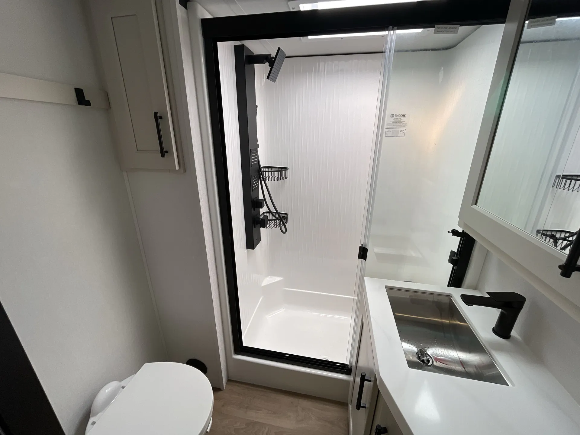 2026 Grand Design Solitude 391DL — Bathroom with a glass-enclosed shower, toilet, vanity sink, black faucet, and mirrored cabinet