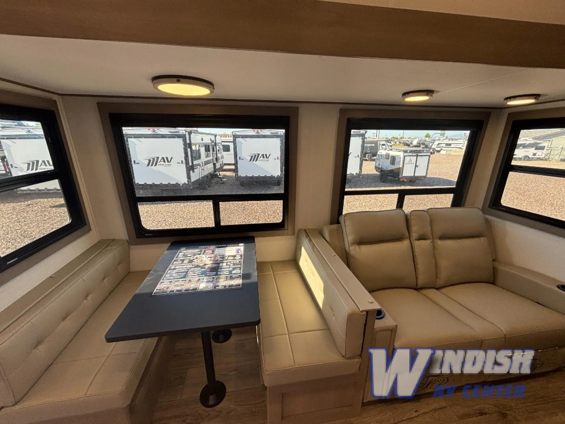 2027 Grand Design Reflection 362TBS — Dinette table between a booth bench and reclining sofa beneath wide RV windows