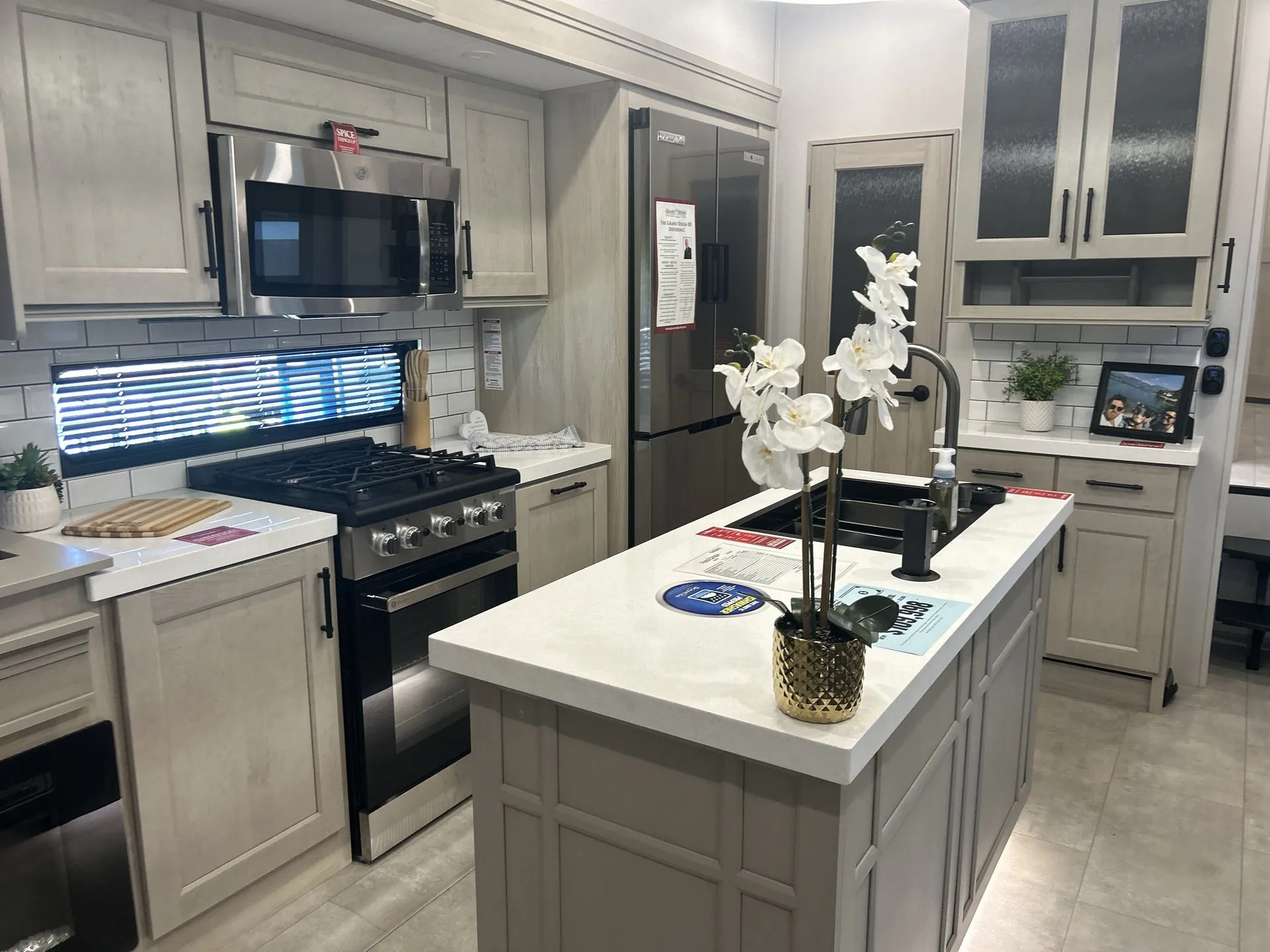 2026 Grand Design Solitude 391DL — Fifth wheel kitchen with island sink, gas range, microwave, refrigerator, and surrounding cabinetry