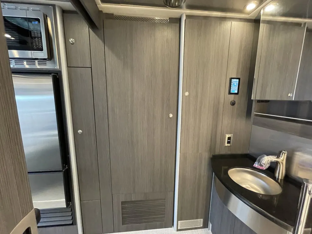 2026 Airstream Atlas Murphy Suite — Class B kitchen with refrigerator, microwave, tall cabinetry, countertop, sink, and wall control panel