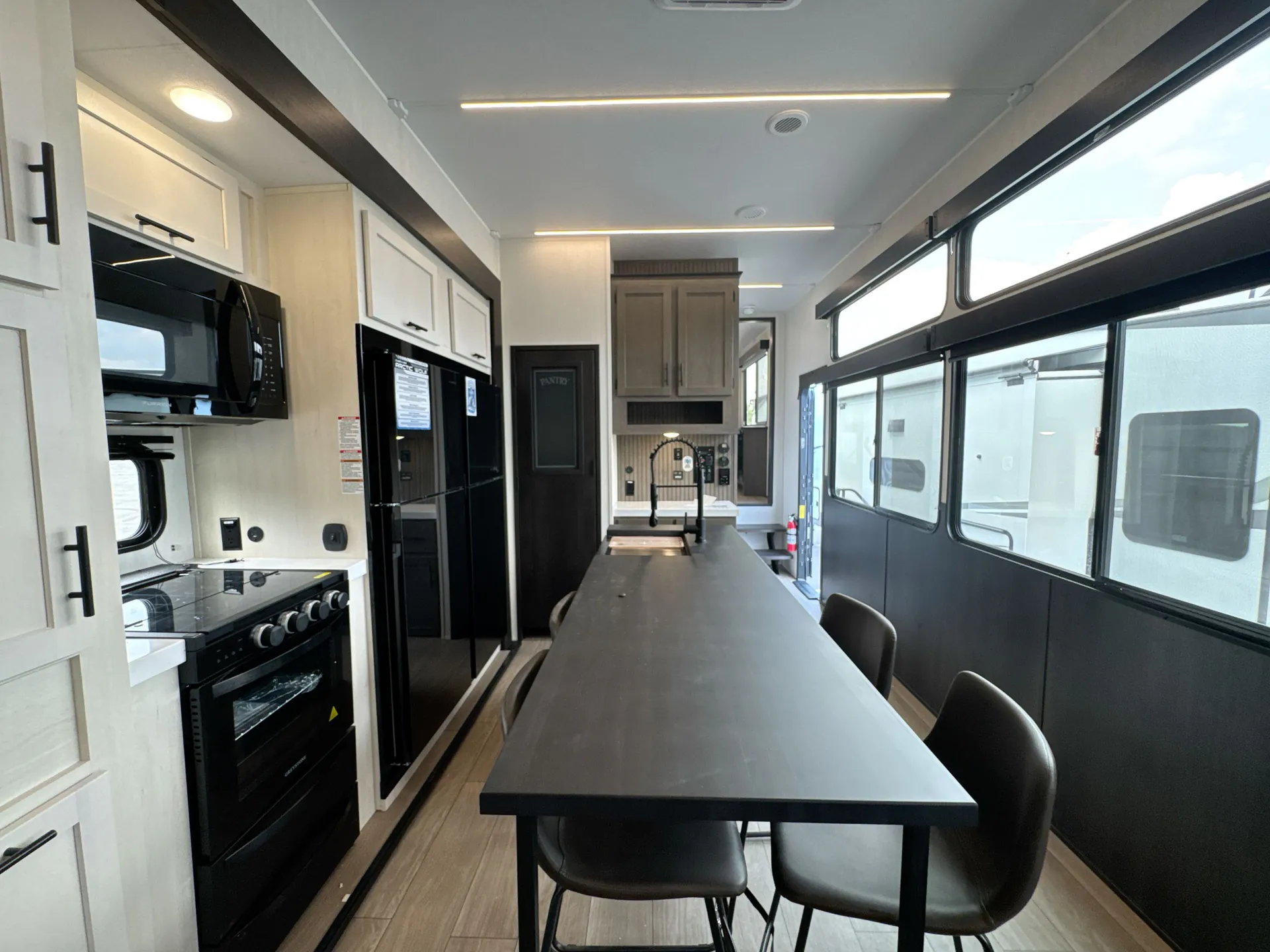 2026 Forest River Arctic Wolf 38LEAH.G — Fifth-wheel dining table and chairs beside a kitchen island, sink, range, refrigerator, and panoramic windows