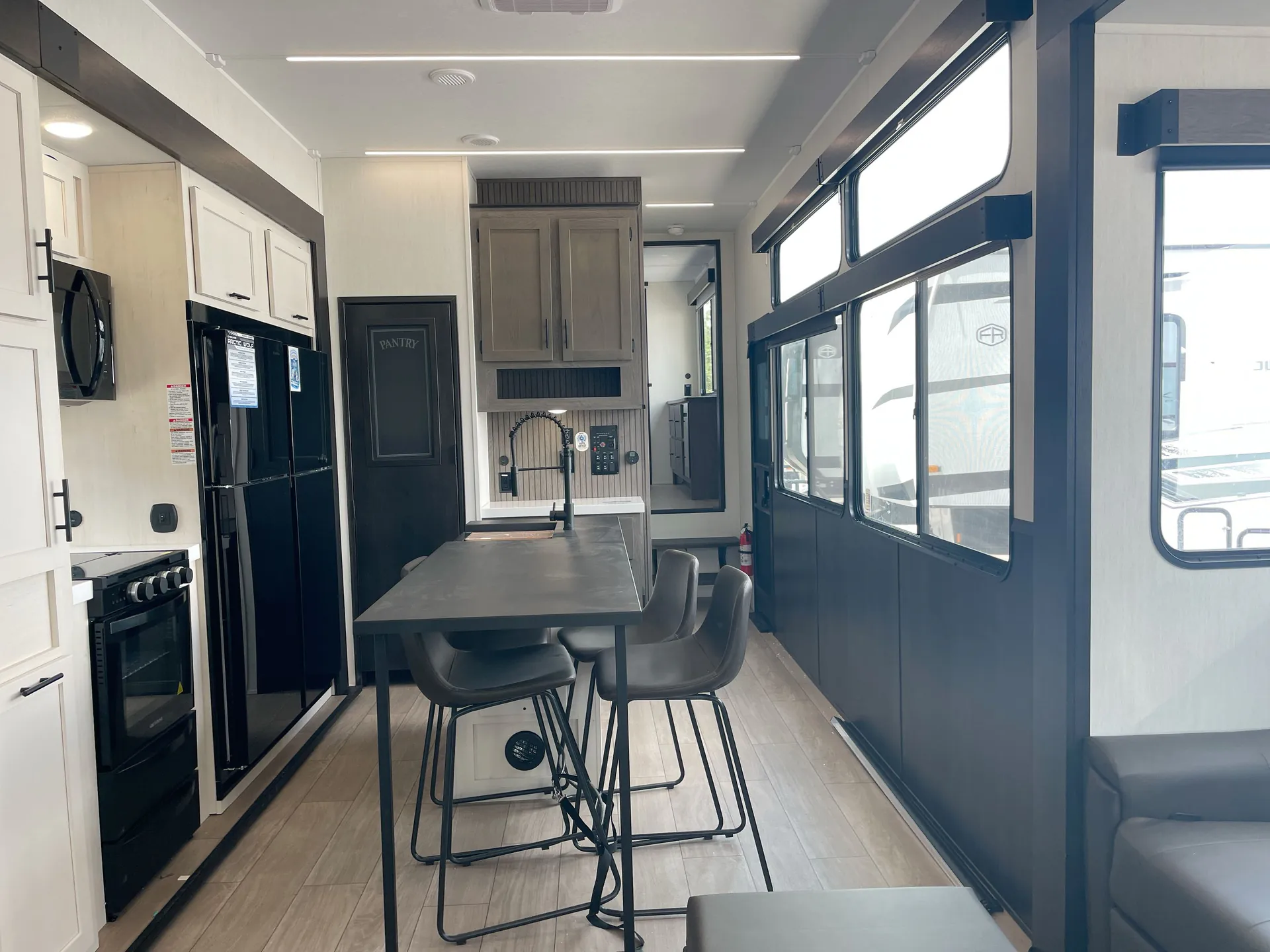 2026 Forest River Arctic Wolf 38LEAH.G — Dining table and chairs centered between the kitchen appliances and cabinetry, with lounge seating visible beside the windows