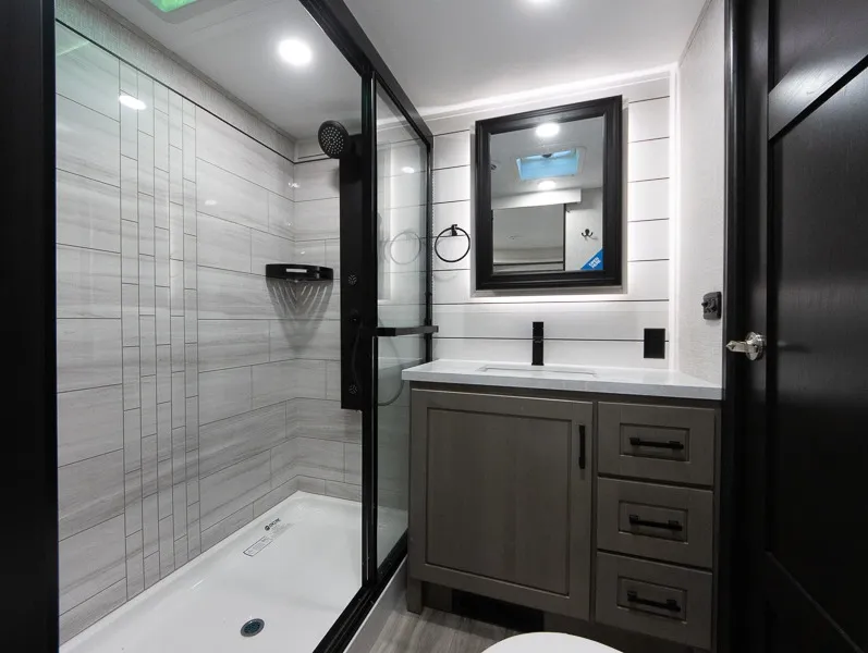 2025 Jayco Seismic Luxury Series 4113 — Bathroom shower with glass enclosure, tiled walls, shower fixtures, vanity, mirror, and toilet edge