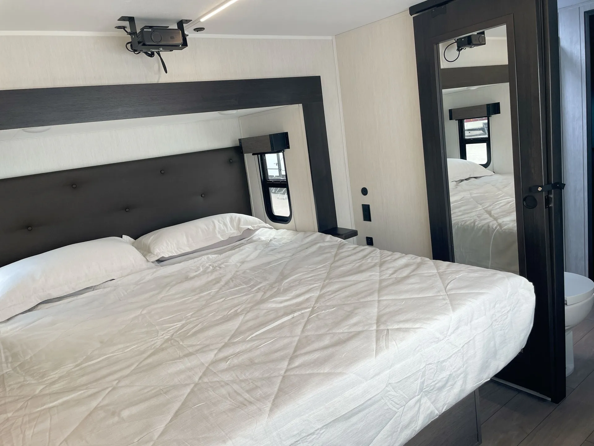 2026 Forest River Arctic Wolf 38LEAH.G — Main bedroom with a large bed, upholstered headboard, bedside shelves, windows, and mirrored wardrobe door