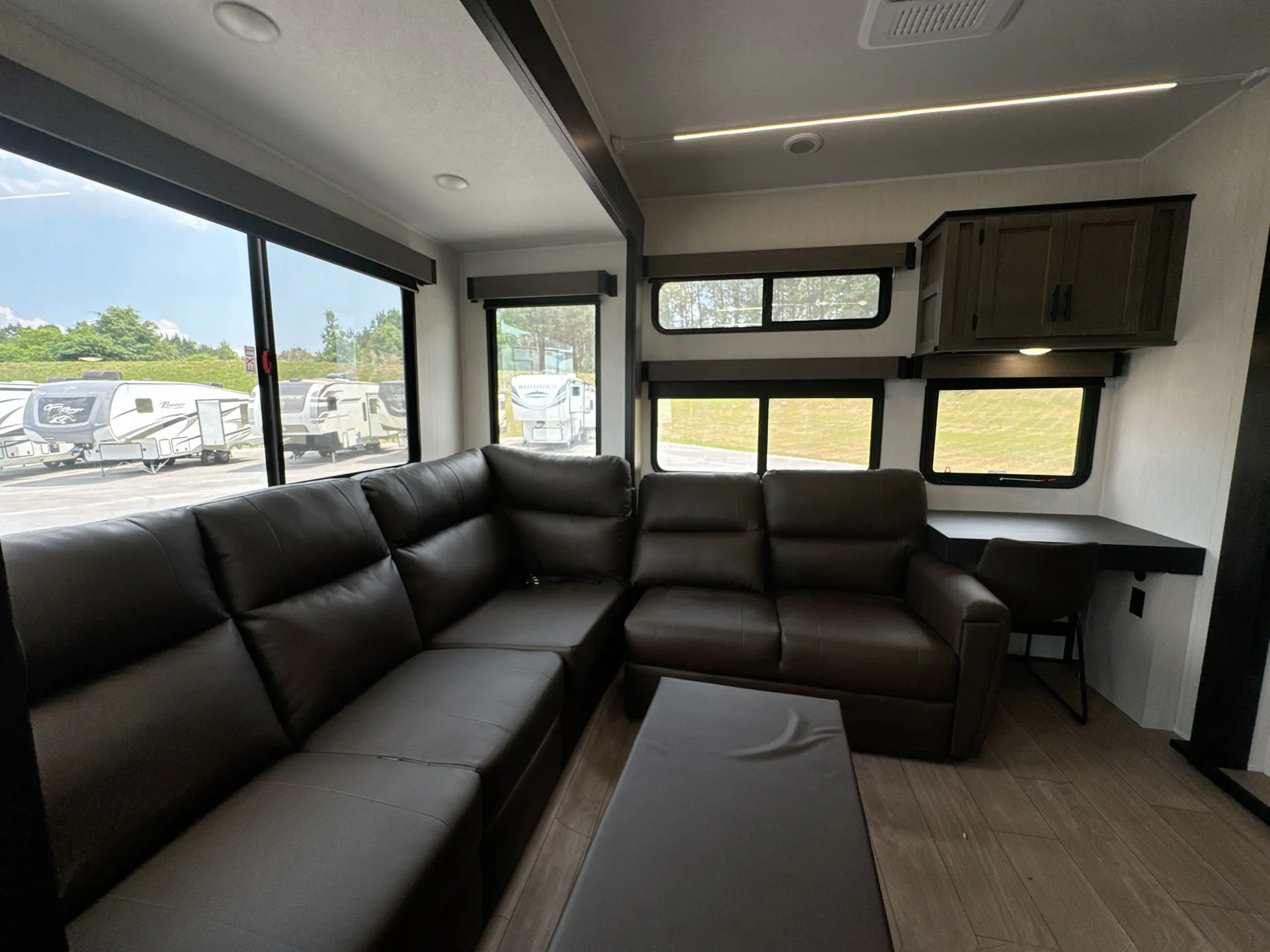 2026 Forest River Arctic Wolf 38LEAH.G — Fifth-wheel living room with sectional sofa, recliners, coffee table, and a small desk beneath multiple windows