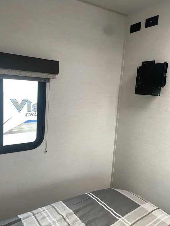 2026 Gulf Stream Vista Cruiser 19ERD — Bedroom corner with the bed, side window, wall-mounted television bracket, and small upper controls