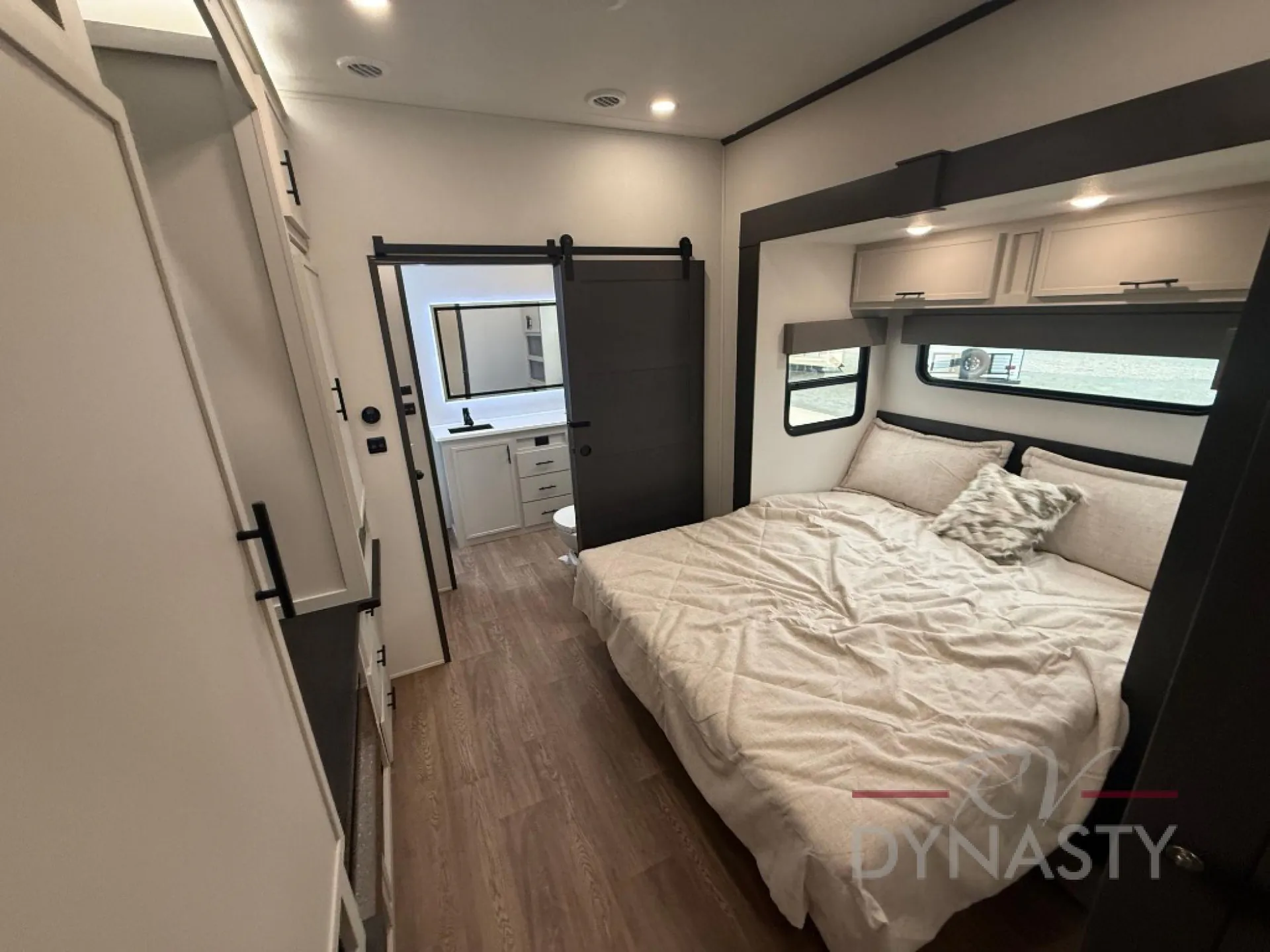2027 Forest River Sanibel 40BUNK — Main bedroom with a made bed, overhead cabinets, side wardrobe, and open view toward the bathroom vanity