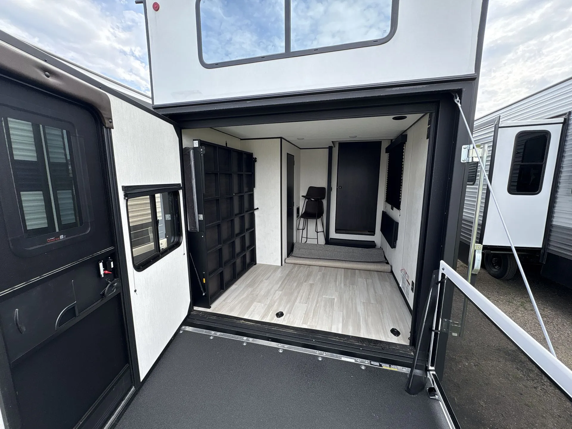 2026 Forest River Cherokee Wolf Pack 397STAY — Open travel trailer garage with broad flooring, tie-down points, wall storage, foldable seating, and rear ramp door