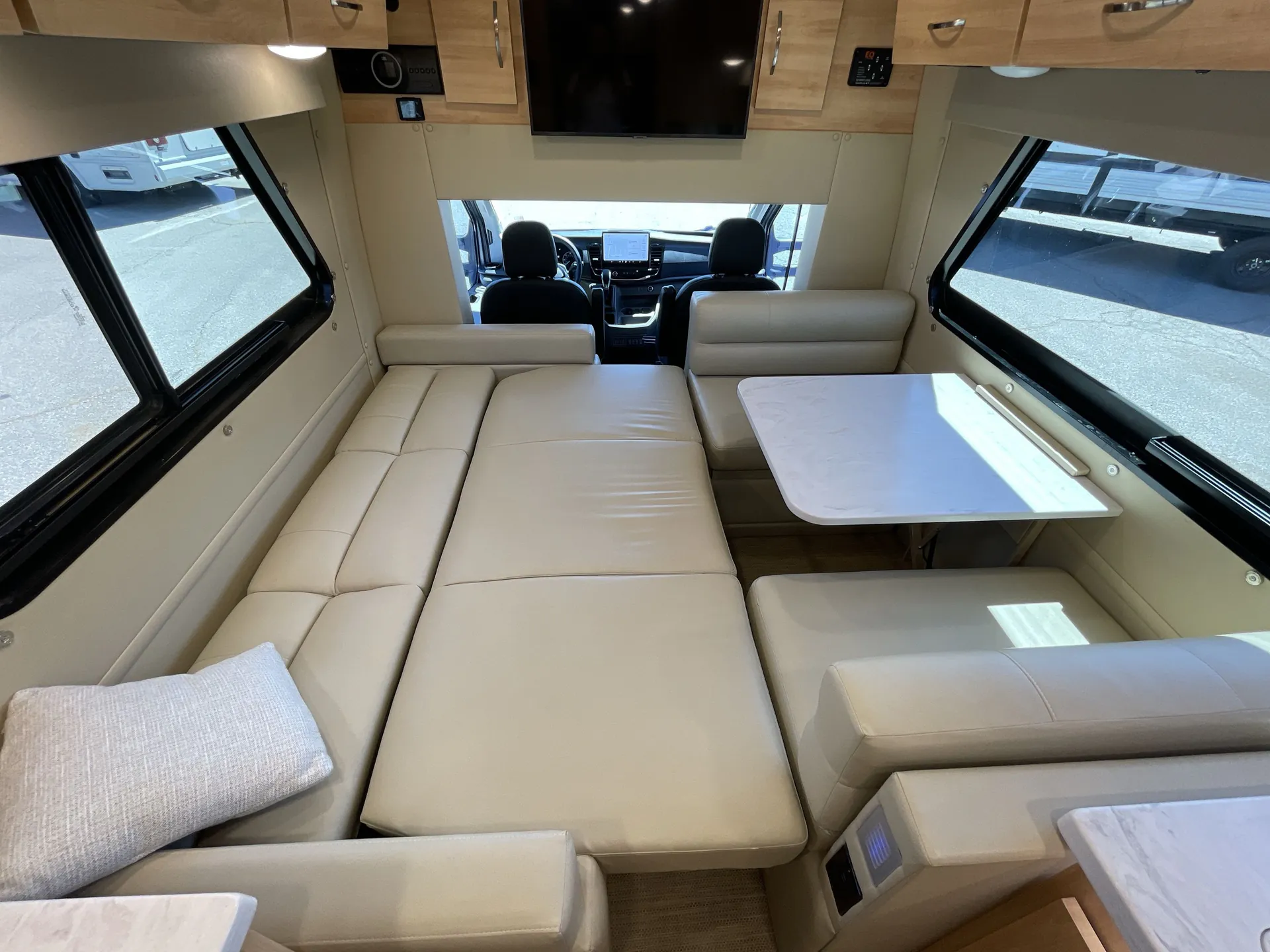2024 Chinook RV Maverick SS — Class B van lounge converts into a broad bed beside a dinette table, with the front cockpit visible beyond