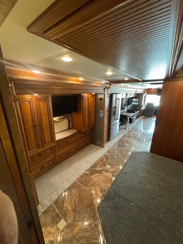 2016 Newmar Dutch Star 4369 — Motorhome lounge with television cabinetry and seating area extending toward the bedroom and rear hallway
