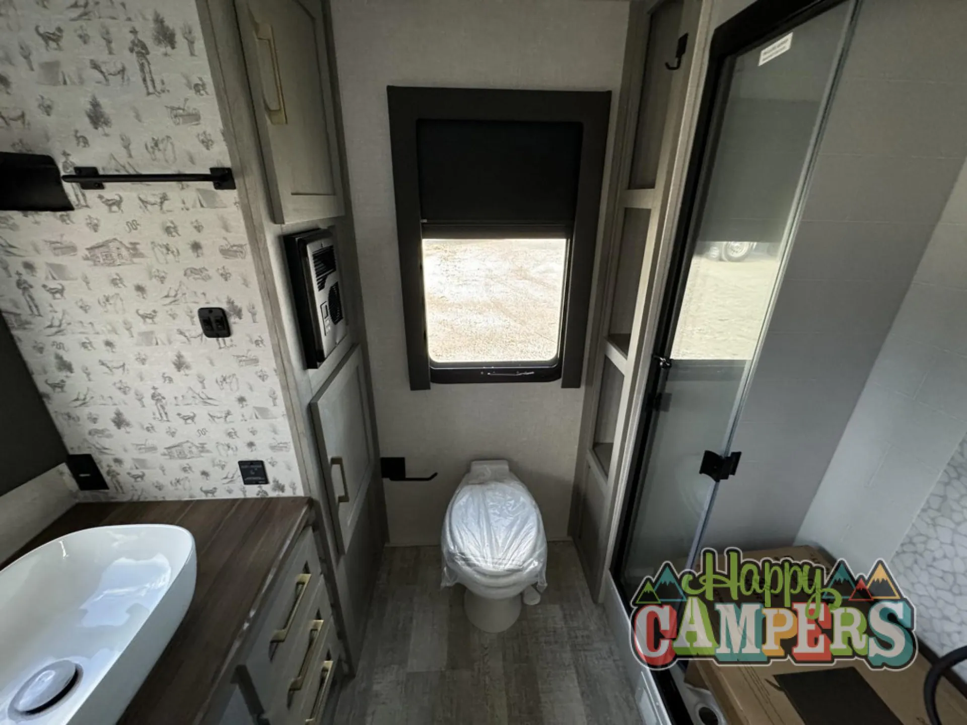 2025 Forest River IBEX RVS3 — Travel trailer bathroom showing a toilet, vanity edge, storage cabinetry, and glass shower enclosure