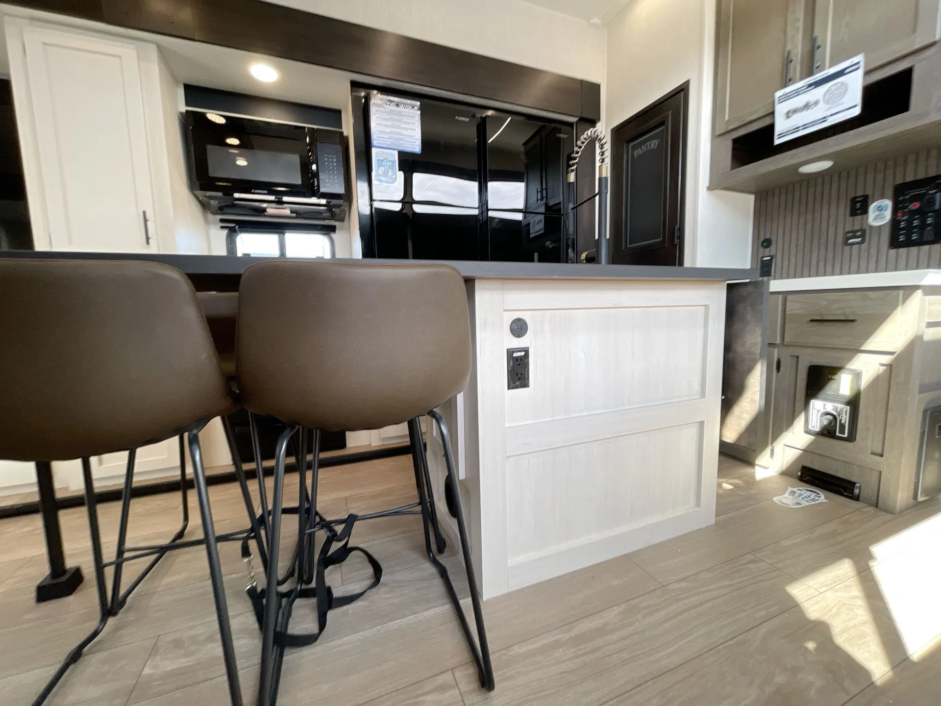 2026 Forest River Arctic Wolf 38LEAH.G — Kitchen peninsula with refrigerator, microwave, sink, cabinetry, and two bar stools at the counter