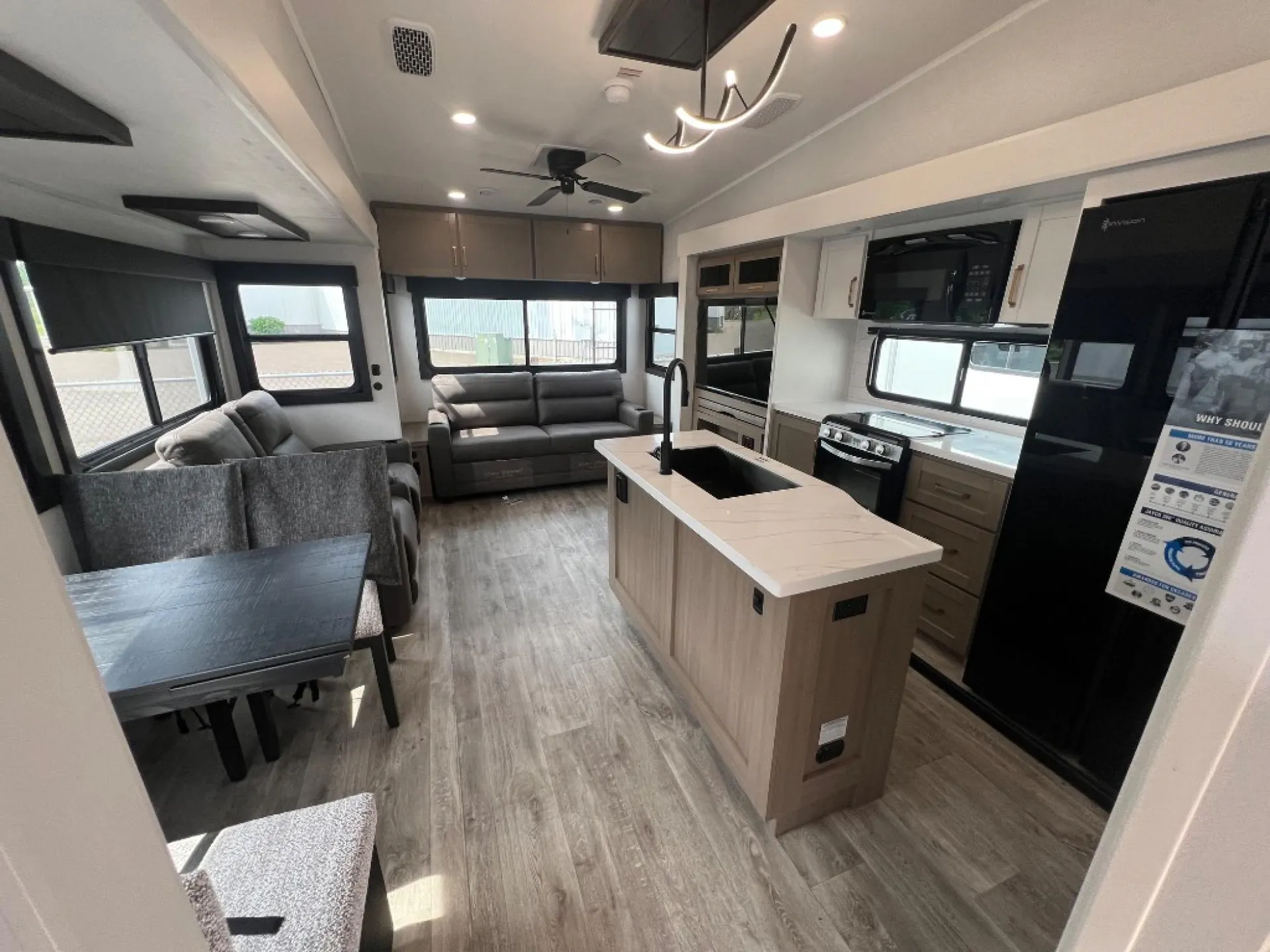 2027 Jayco Eagle 355MBQS — Kitchen island with sink and appliances overlooks a lounge, recliners, and freestanding dining table in the fifth wheel interior