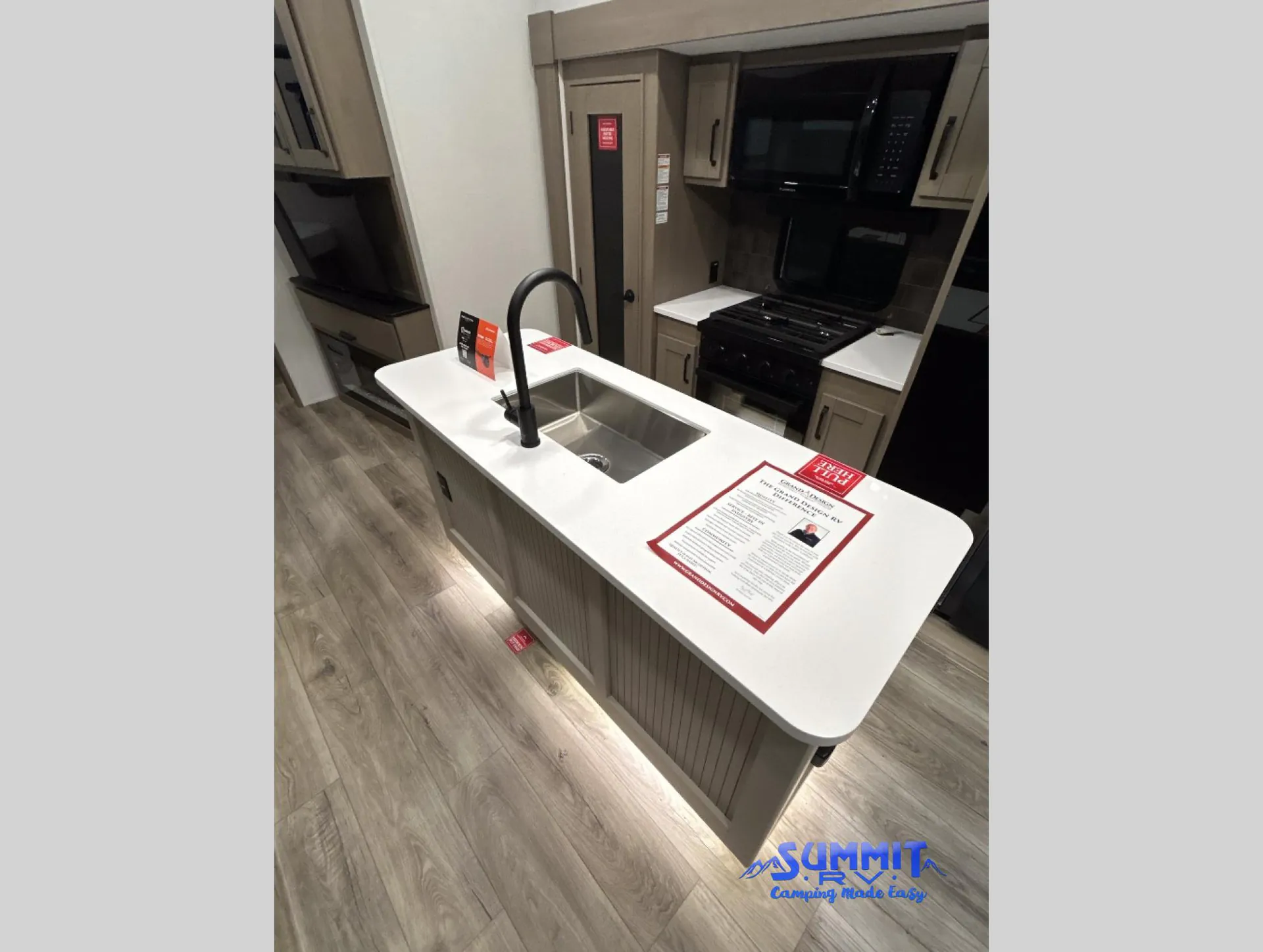2027 Grand Design Reflection 362TBS — Kitchen island with double sink and faucet facing a range, microwave, refrigerator, and adjacent entertainment seating