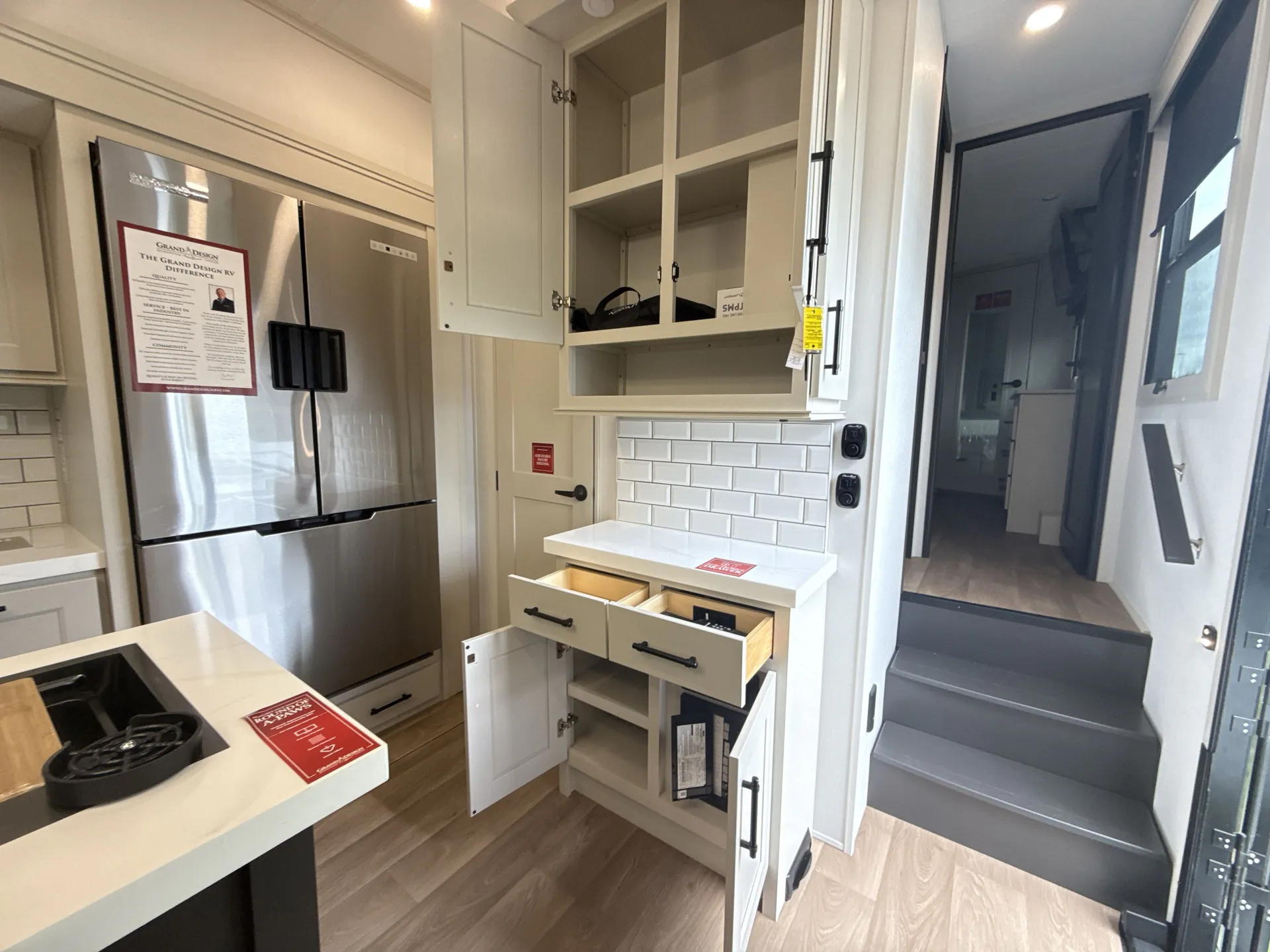 2026 Grand Design Solitude 391DL — Fifth wheel kitchen storage wall with open cabinets, drawers, counter, refrigerator, island edge, and entry steps