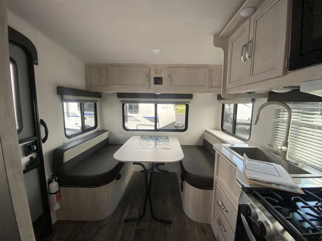 2026 Gulf Stream Vista Cruiser 19ERD — Travel trailer dinette with facing benches, table, windows, and adjacent kitchen sink, cabinets, and range