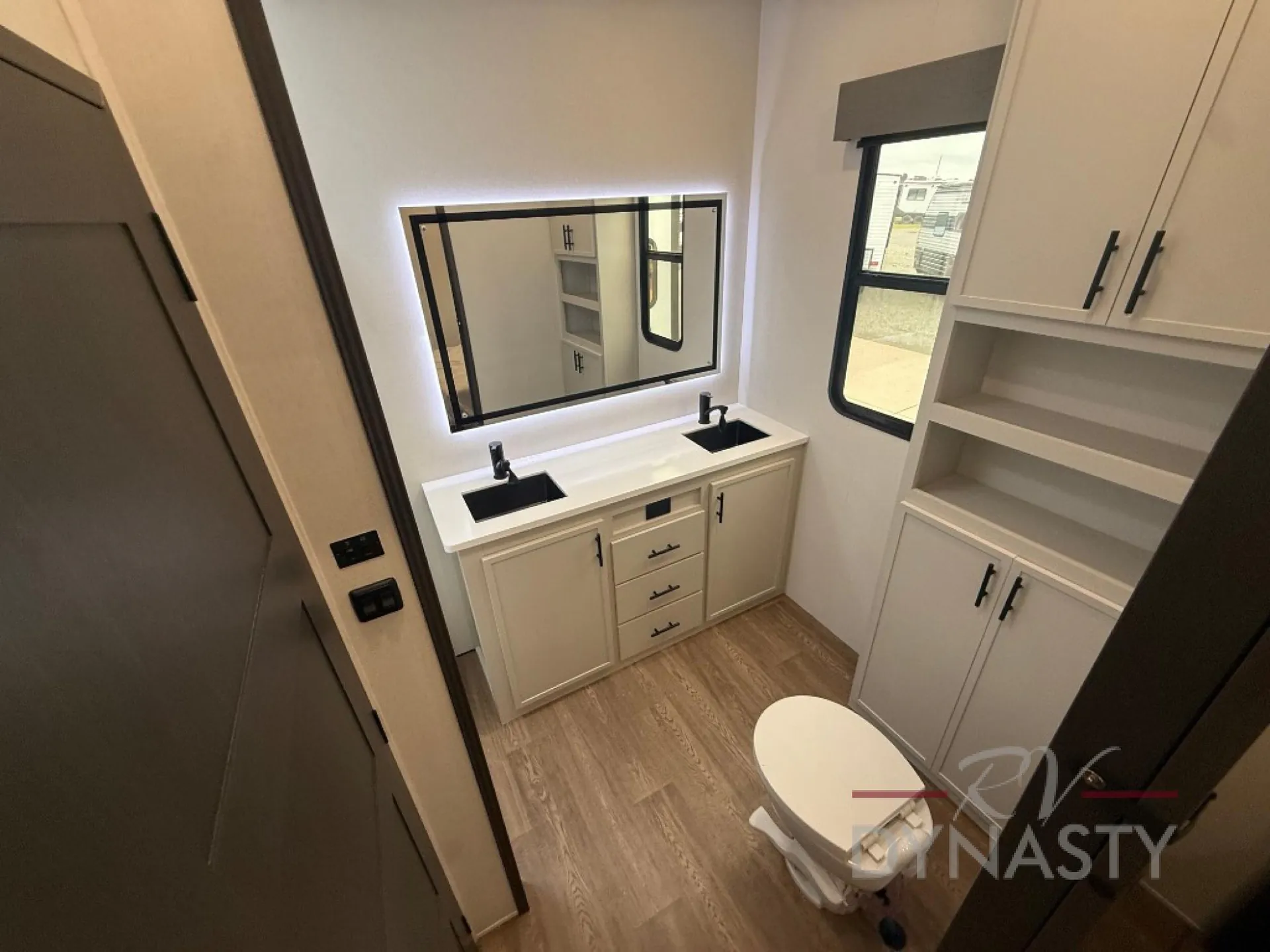 2027 Forest River Sanibel 40BUNK — Bathroom with double-sink vanity, illuminated mirror, toilet, window, and extensive surrounding storage cabinetry