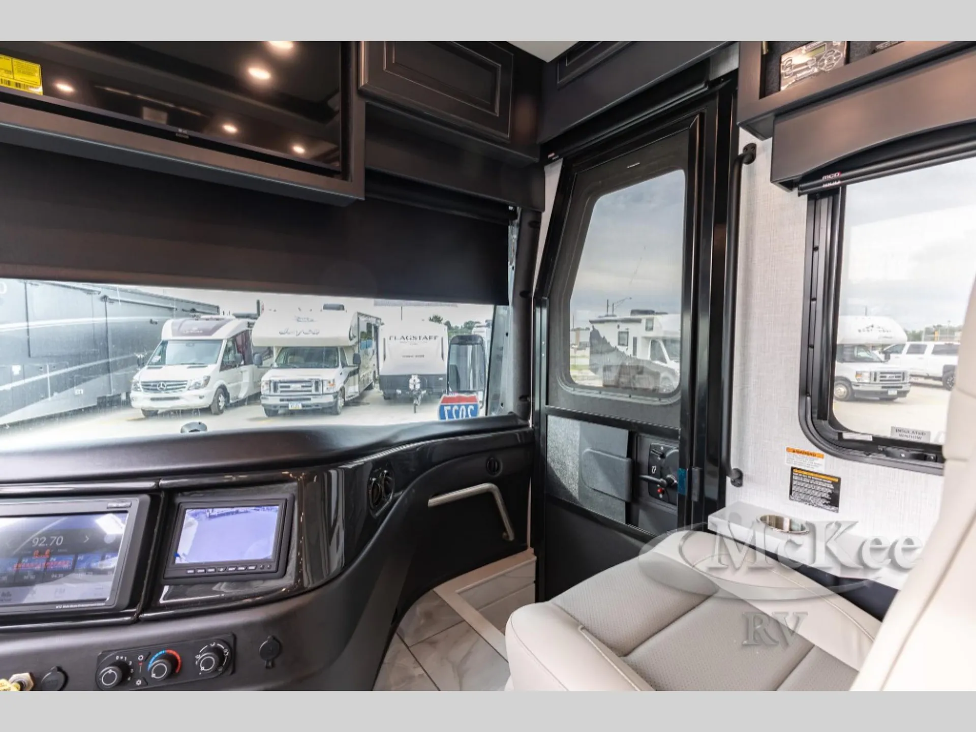 2027 Fleetwood Discovery LXE 40M — Class A motorhome passenger-side cockpit with dashboard displays, entry door, windshield, and passenger seat
