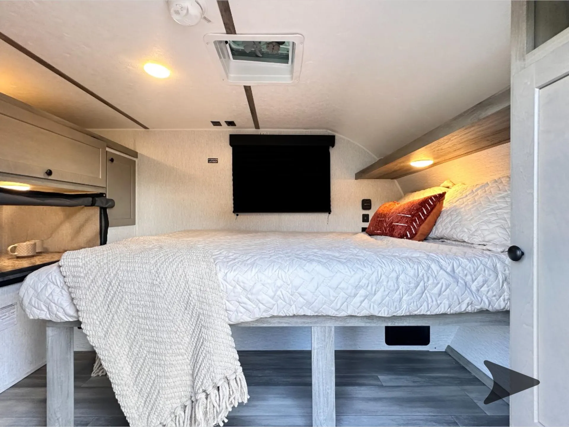 2026 Wayfinder Go Lite Solo — Main bed with quilted bedding, wall shade, side cabinets, overhead shelf, bedside controls, and under-bed storage