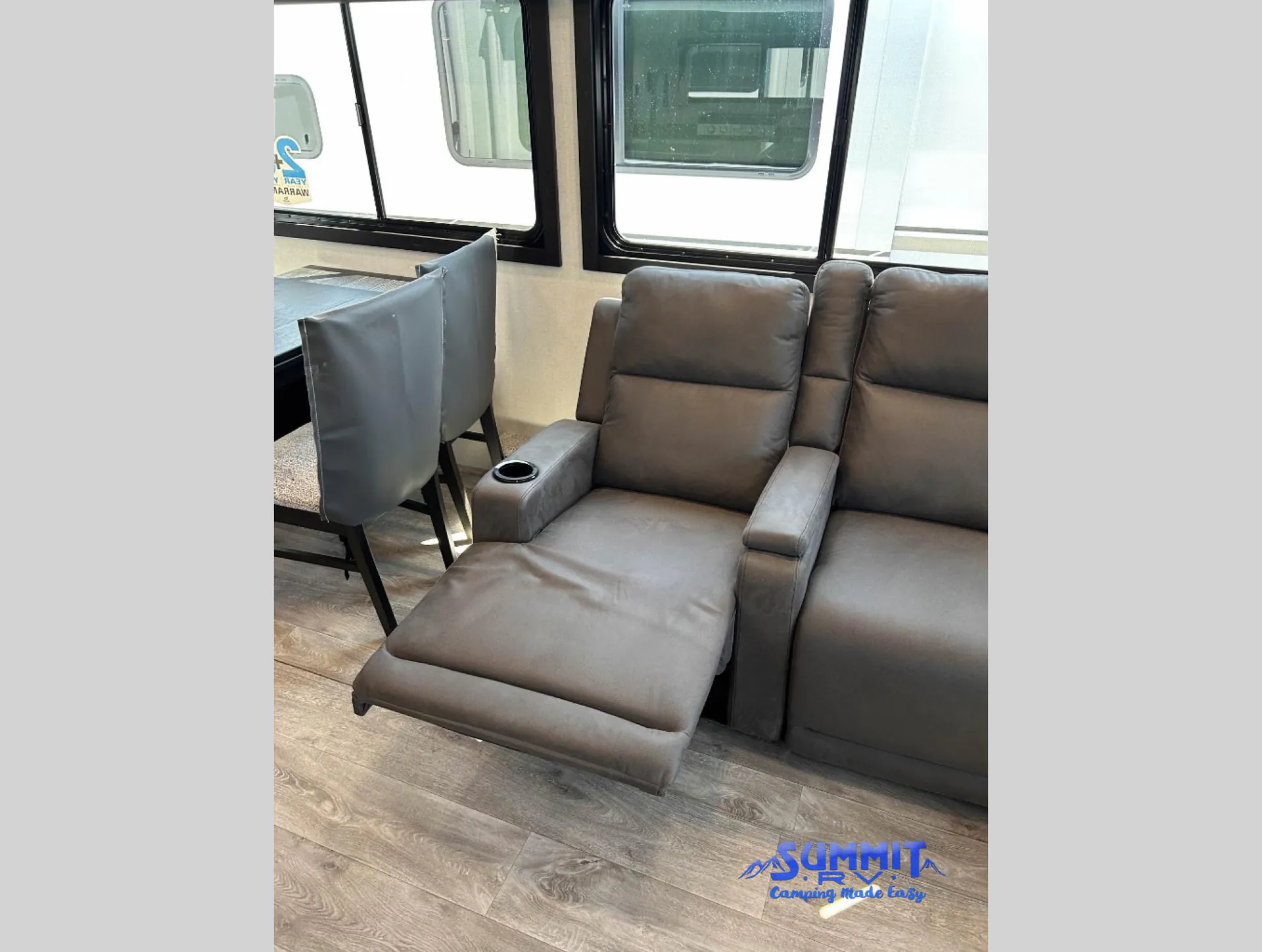 2027 Jayco Eagle 355MBQS — Living area showing an extended theater recliner beside a freestanding dining table and chairs