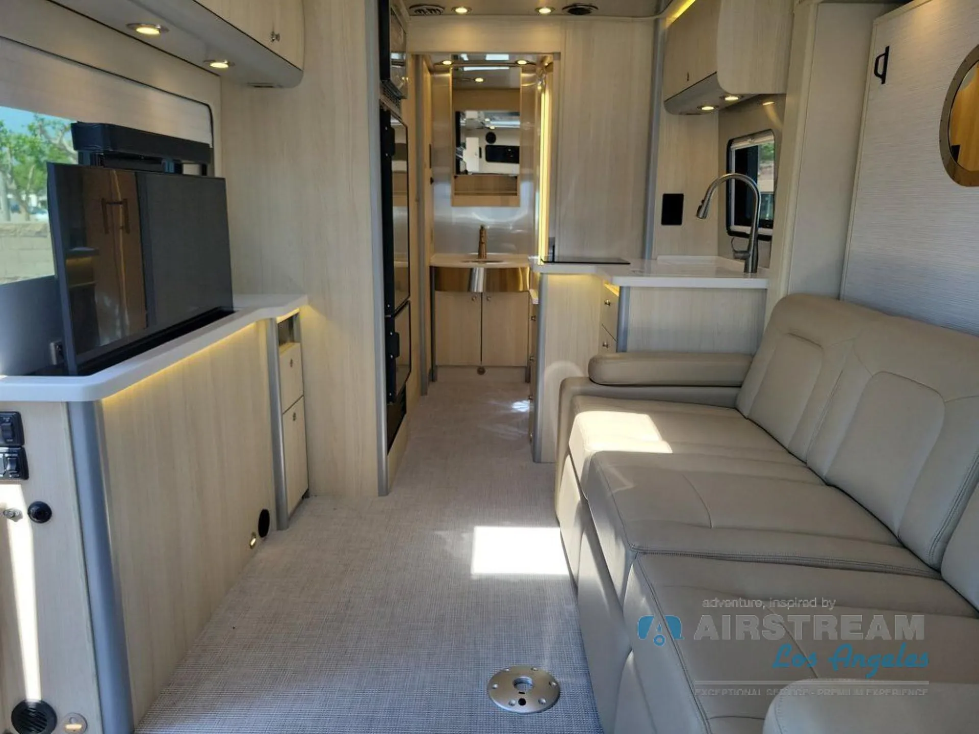 2026 Airstream Atlas Murphy Suite — Class B van interior with a leather sofa, television, galley sink and counter, and rear seating area