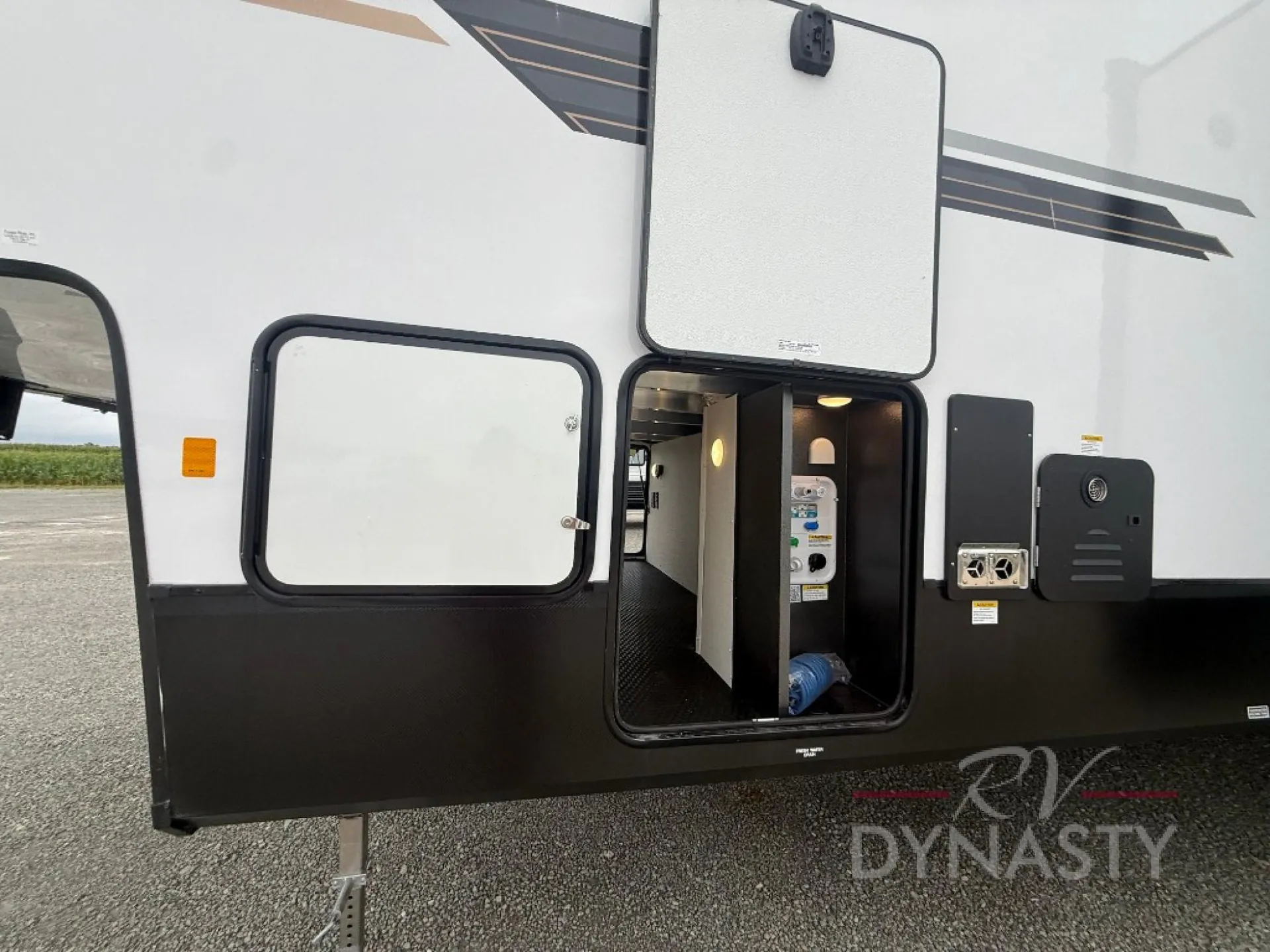 2027 Forest River Sanibel 40BUNK — Exterior side view visibly shows open utility/service compartments and plumbing connections on the RV body