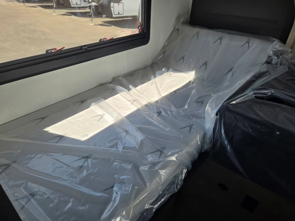2027 Grand Design Lineage Series F 29AN5 — Main bedroom mattress covered in protective plastic beside a large window and upholstered headboard