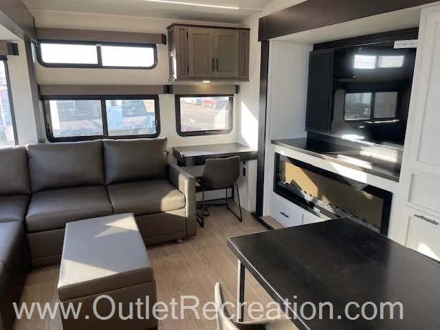 2026 Forest River Arctic Wolf 38LEAH.G — Living room sofa and ottoman beside a dining desk, entertainment center, and kitchen island edge