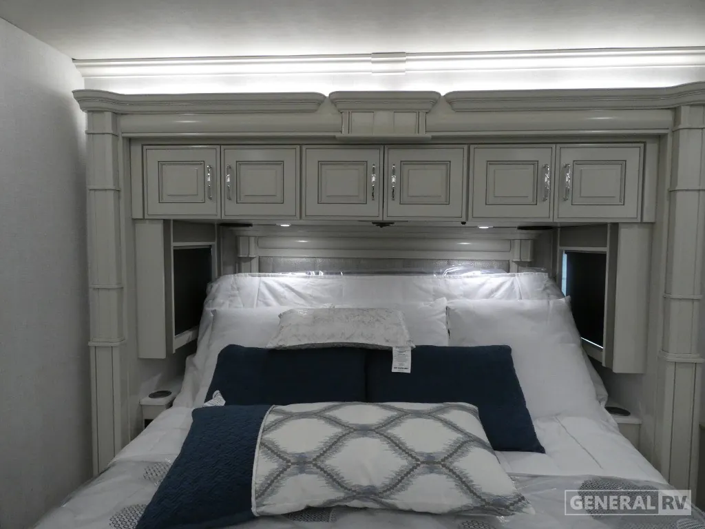 2026 American Coach American Dream 45A — Main bedroom bed with pillows, overhead cabinets, side storage, and decorative wall framing