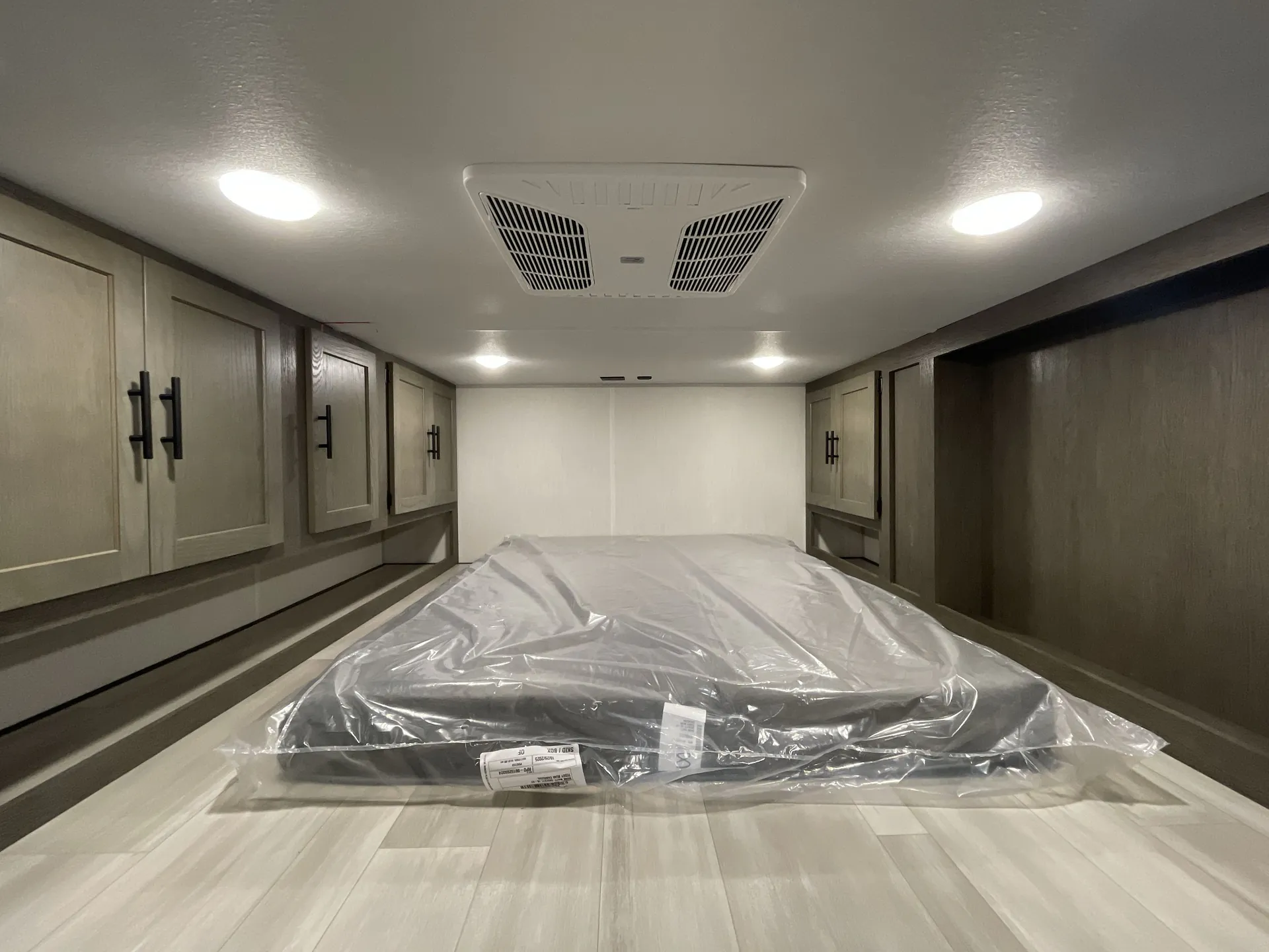 2026 Forest River Cherokee Wolf Pack 397STAY — Travel trailer loft mattress wrapped in protective plastic with overhead vent and cabinets along both sides
