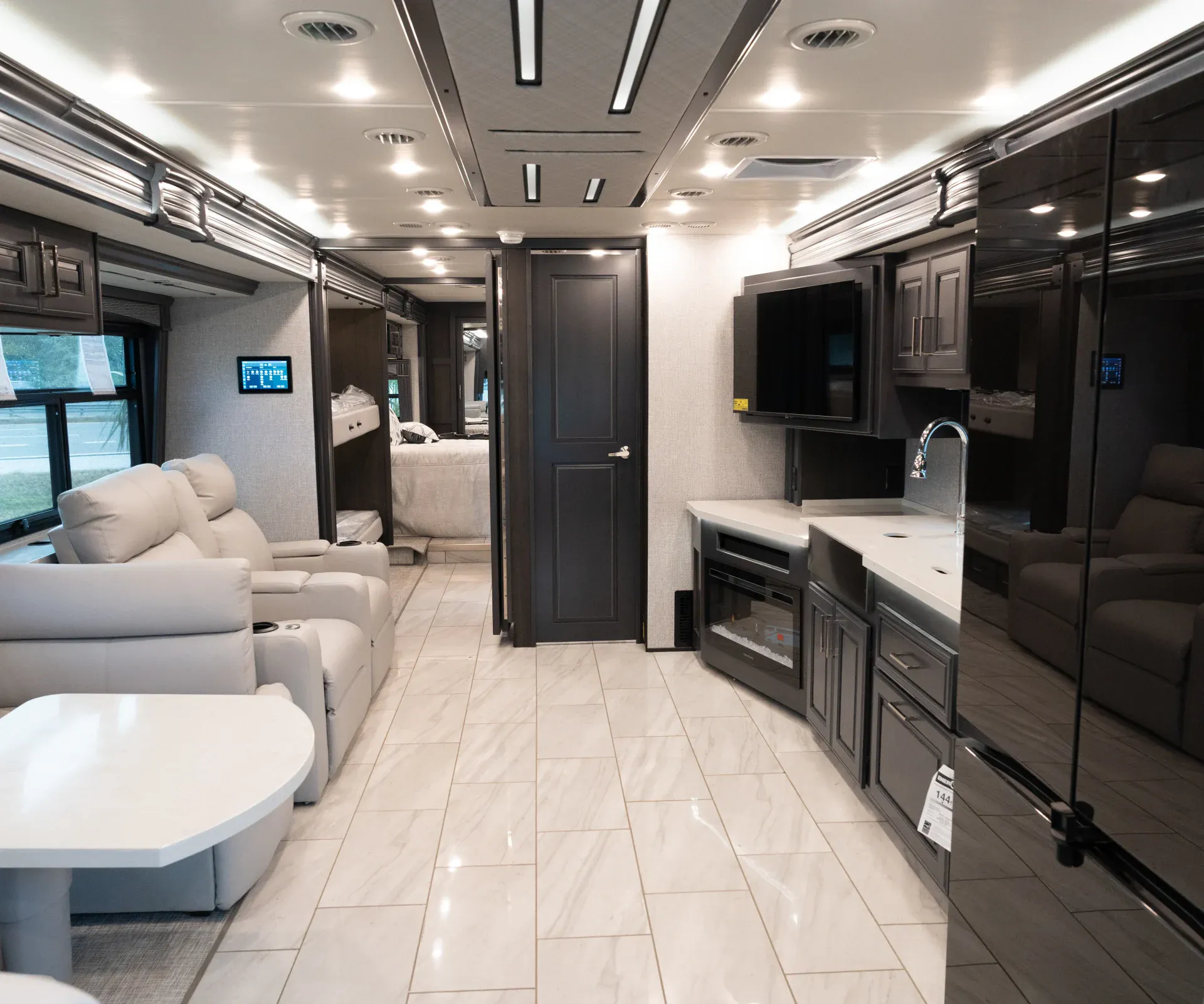2026 Fleetwood Discovery LXE 40G — Interior overview showing lounge seating, kitchen appliances and counter, refrigerator, hallway, and rear bed area