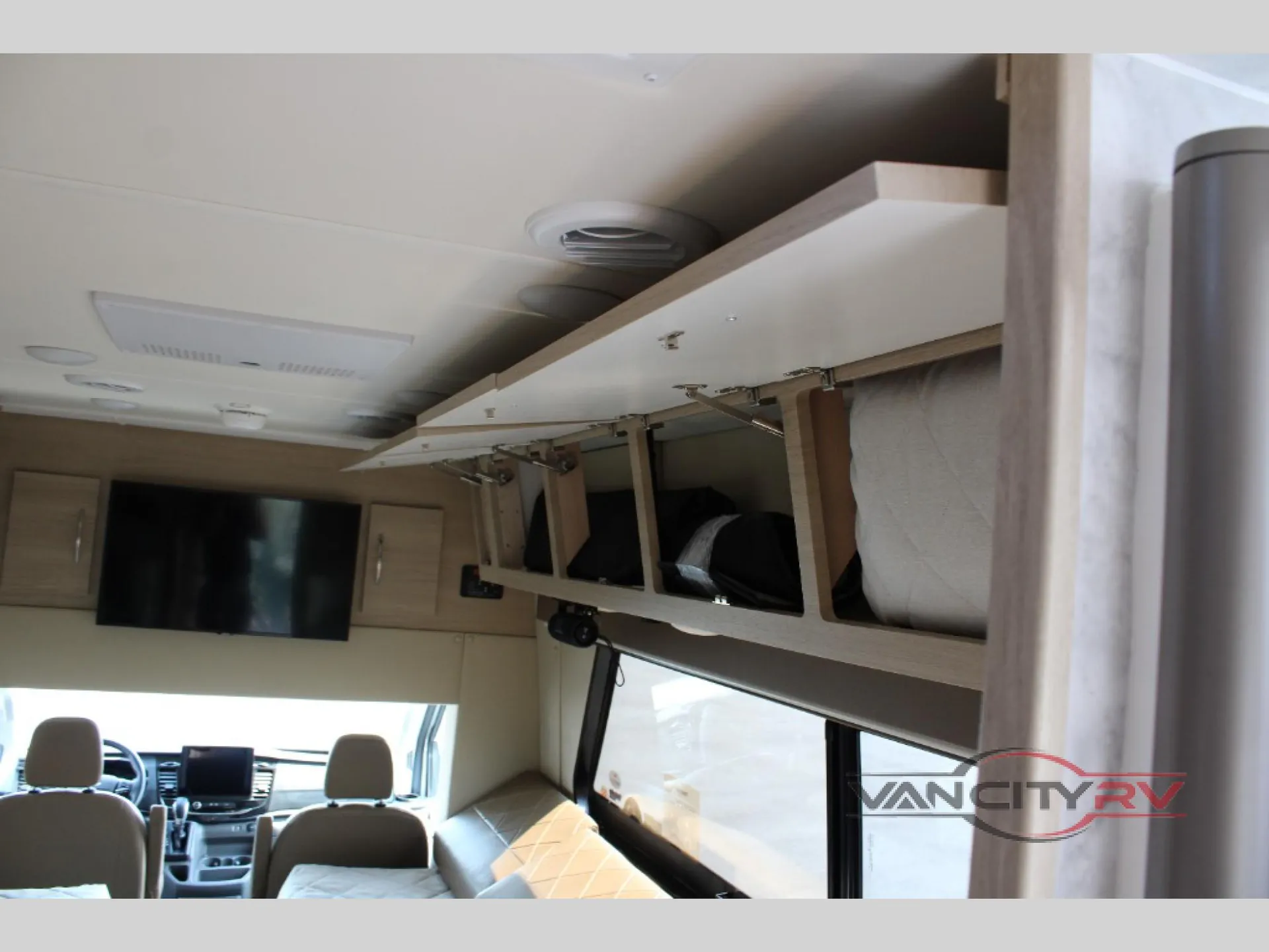 2025 Chinook RV Maverick SS — Open overhead storage above a sleeping surface with the Class B van cockpit visible beyond