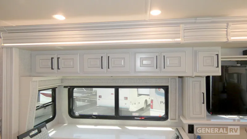 2027 Fleetwood Discovery LXE 40M — Dining nook with a white tabletop, upholstered chair edge, bay window, and surrounding overhead cabinetry