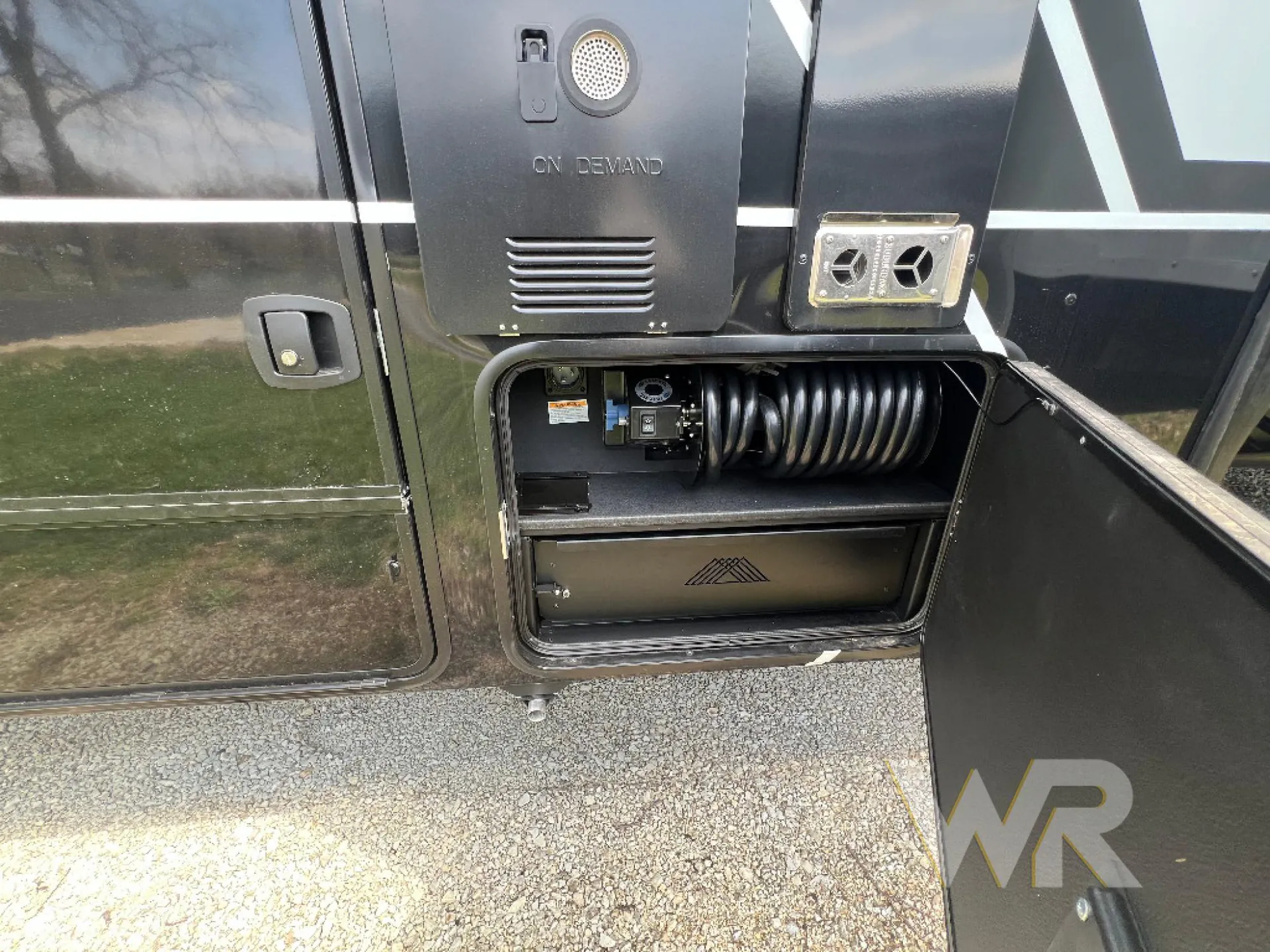 2026 Brinkley Model G 3950 — Open exterior compartment visibly contains utility/service equipment and a coiled hose on the RV exterior