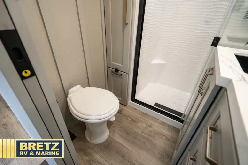 2026 Brinkley Model G 3950 — Fifth wheel bathroom with a toilet, enclosed shower, storage cabinet, and wood-look flooring