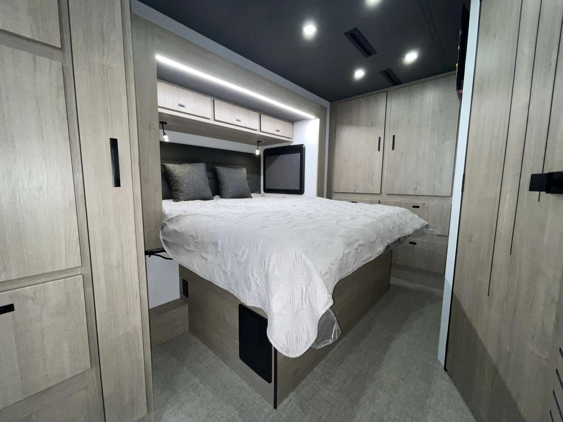 2027 Grand Design Lineage Series F 31ZW — Main bedroom with a made bed, overhead cabinets, wardrobes, side windows, and surrounding storage