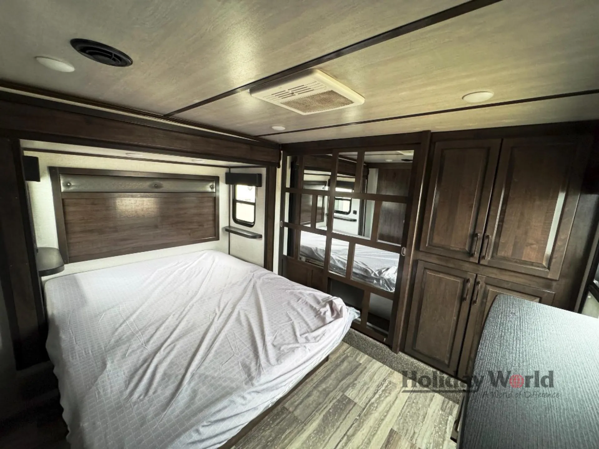 2022 Dutchmen Voltage 4225 — Main bedroom with bed, padded headboard, mirrored wardrobe doors, dresser storage, and side window