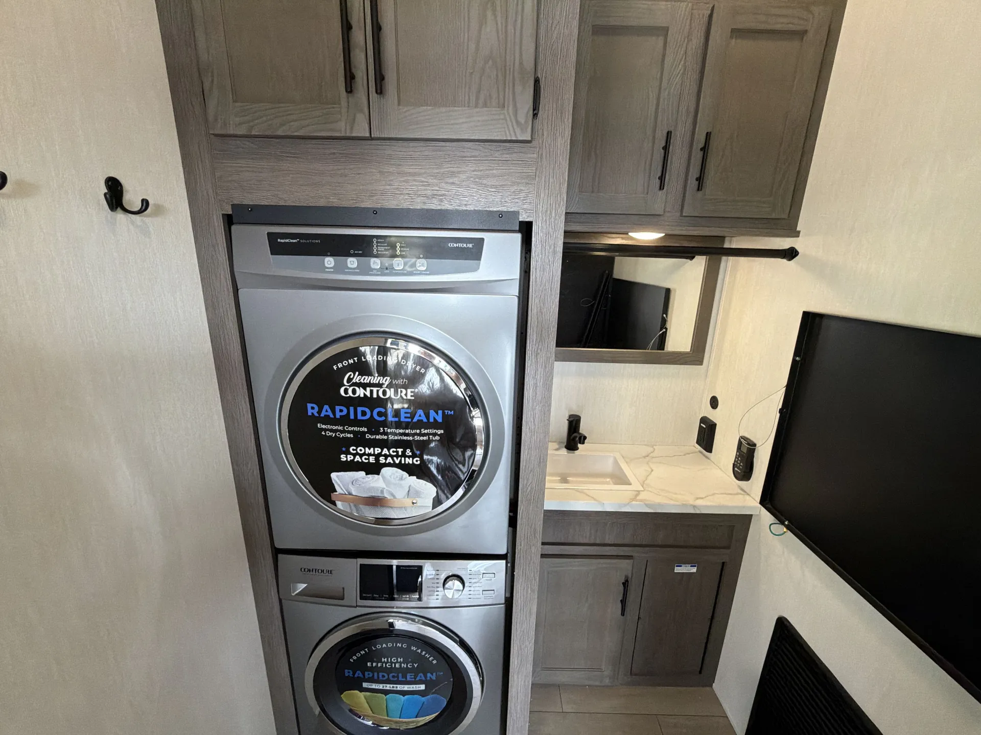 2026 Forest River Arctic Wolf 38LEAH.G — Fifth wheel bathroom showing stacked washer-dryer, sink vanity, mirror, cabinets, and wall-mounted television