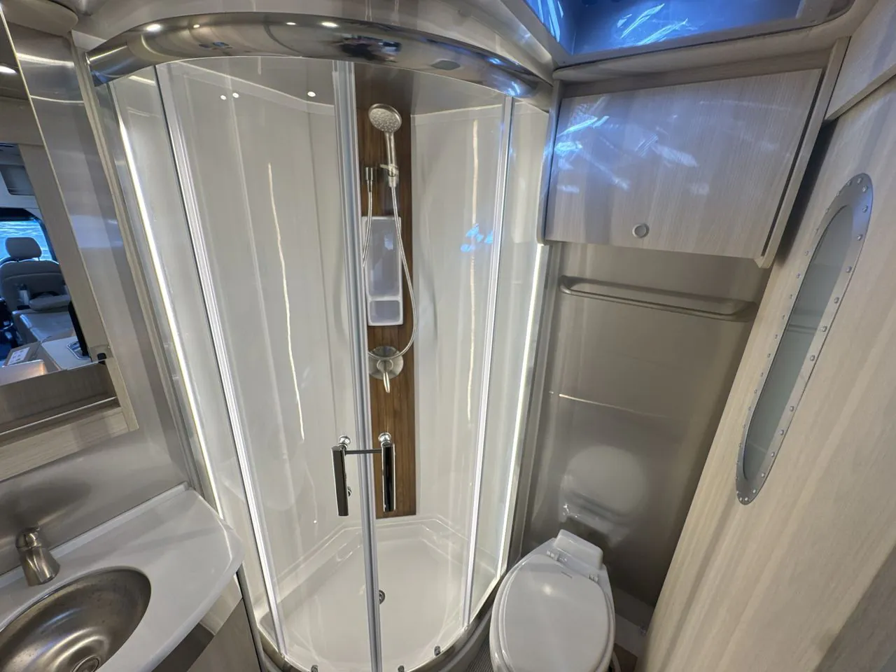 2026 Airstream Atlas Murphy Suite — Glass-enclosed shower beside a toilet, bathroom cabinet, and partial sink vanity