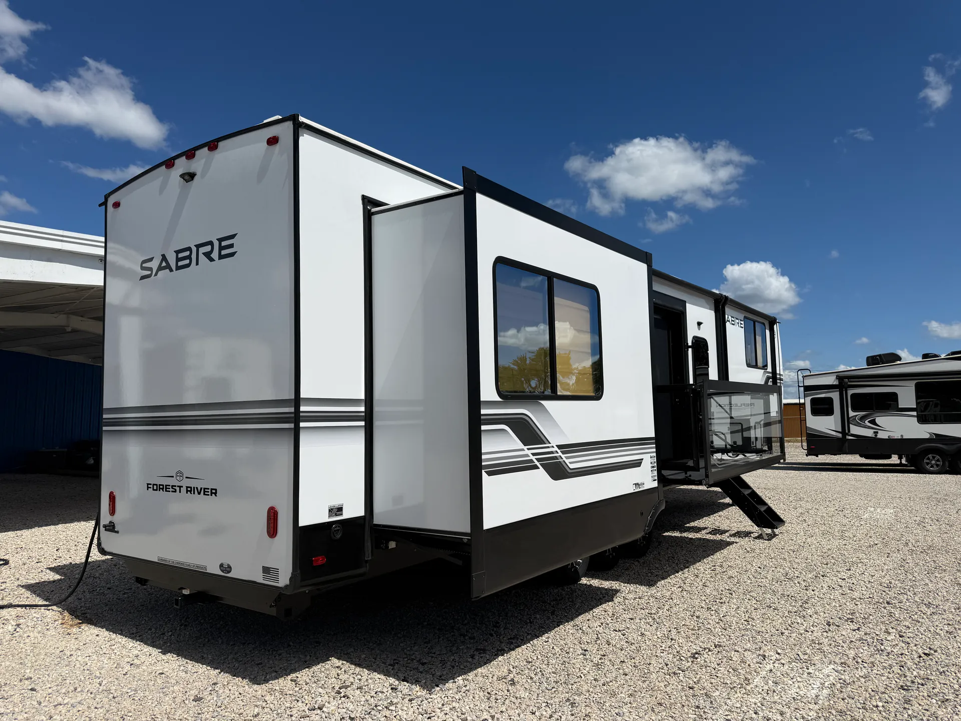 2027 Forest River Sabre 38RVHUNTER — Rear-side outdoor photograph visibly shows the physical RV exterior, rear wall, slide-outs, entry steps, and side windows