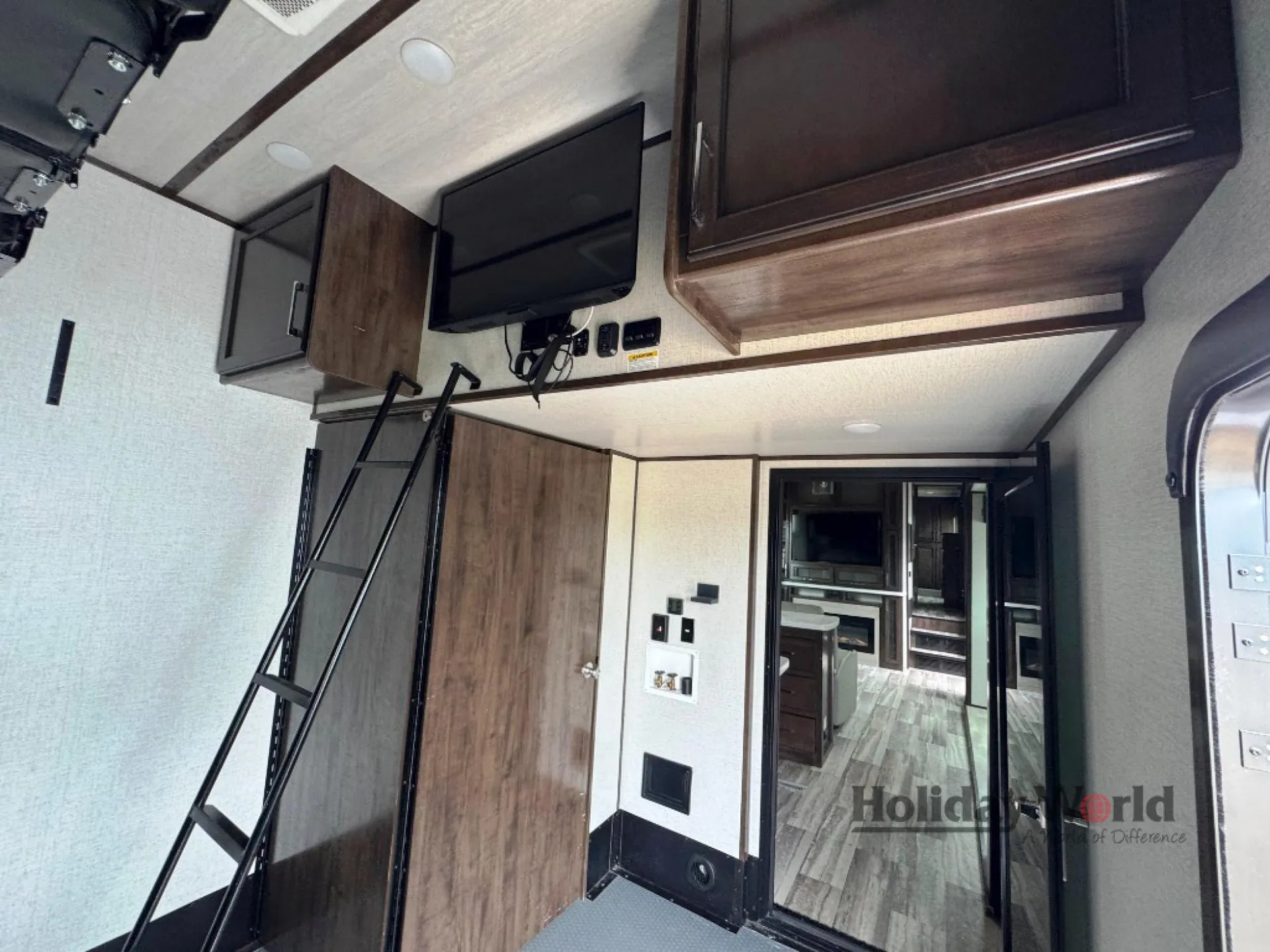 2022 Dutchmen Voltage 4225 — Over-cab loft sleeping platform with ladder, television, surrounding cabinets, and view toward the trailer interior