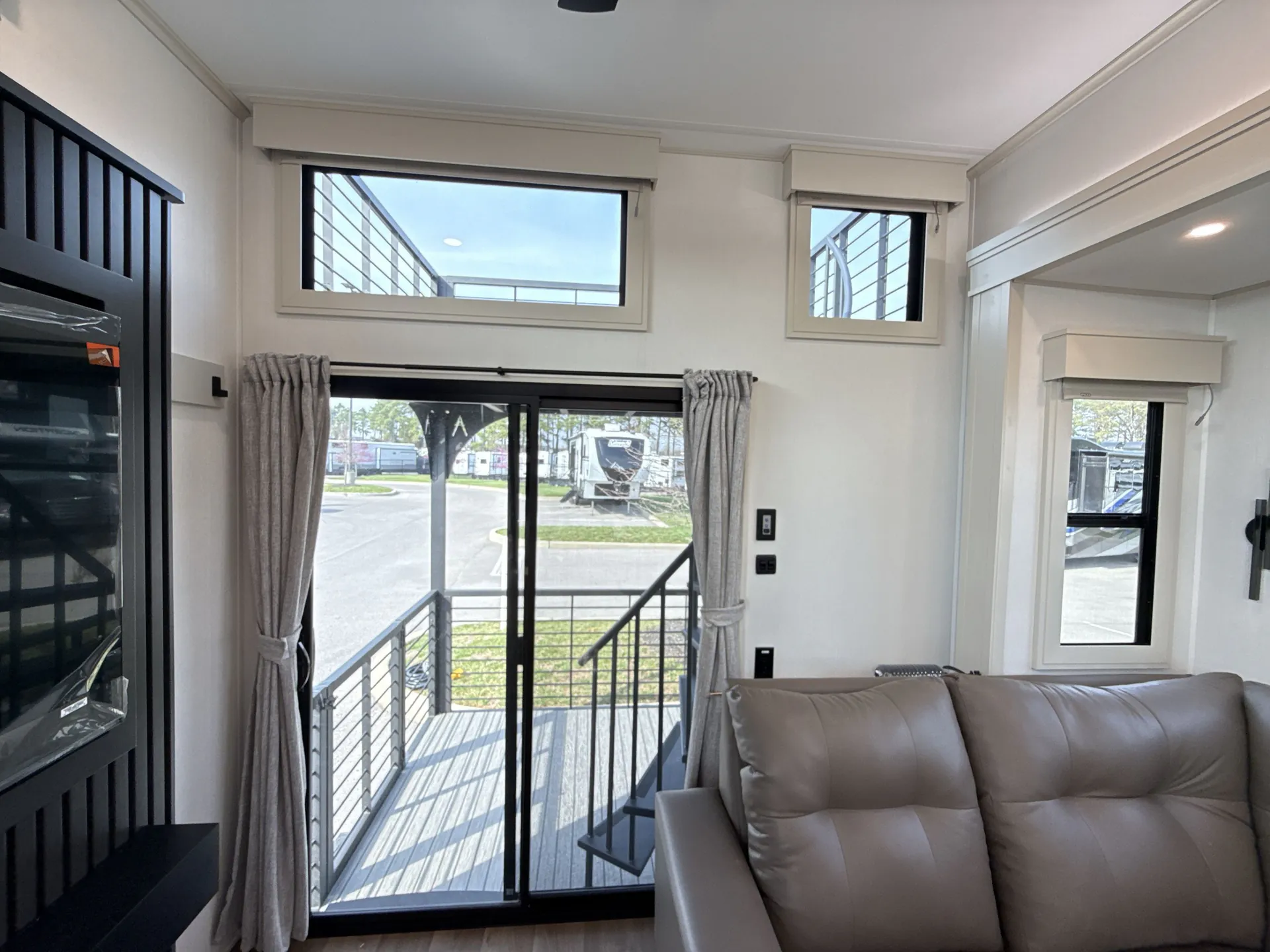 2026 Grand Design Foundation 42GD — Destination trailer living area with leather sofa, entertainment cabinet, and sliding glass door opening to an exterior deck
