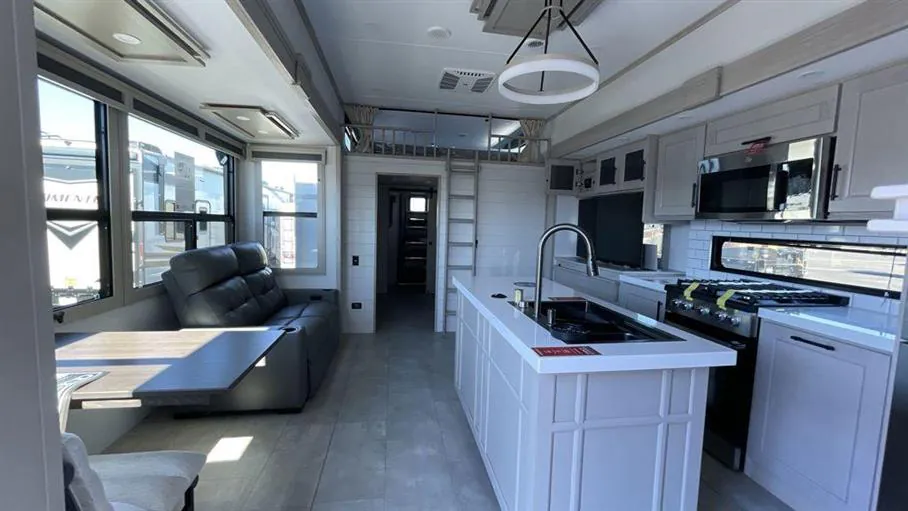 2026 Grand Design Solitude 391DL — Fifth wheel interior overview with kitchen island, range, refrigerator, lounge sofa, and adjacent dinette seating