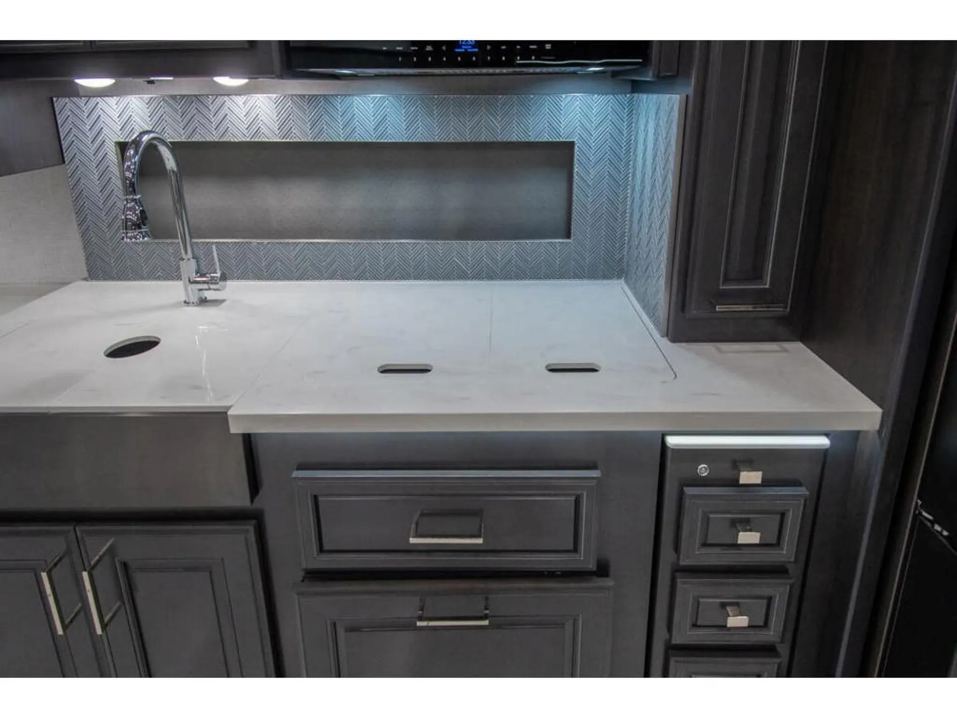 2026 Fleetwood Discovery LXE 40G — Kitchen counter with sink faucet, covered cooktop, backsplash, drawers, and dark cabinetry