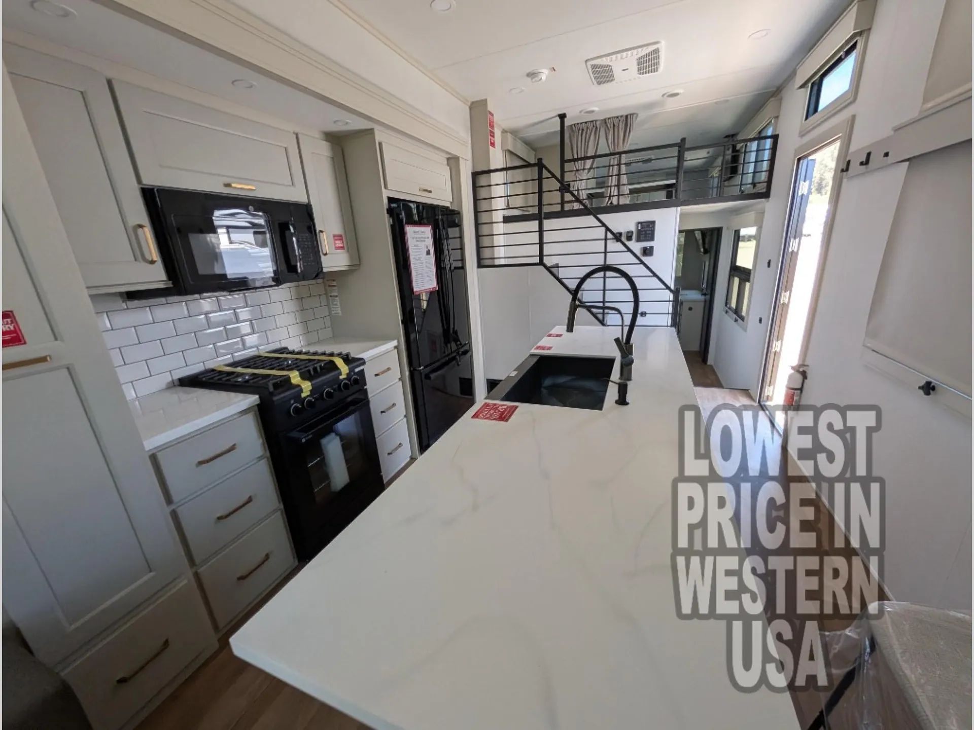 2026 Grand Design Foundation 42GD — Kitchen island sink faces a range, microwave, refrigerator, cabinetry, staircase, and curtained overhead loft