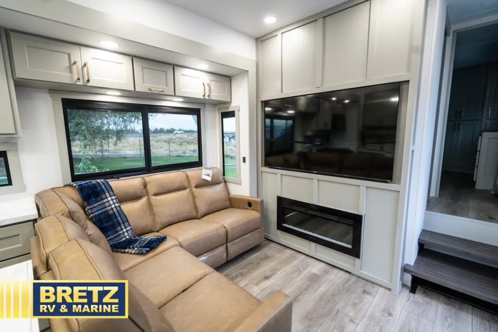 2026 Brinkley Model G 3950 — Fifth wheel lounge with sectional seating, large television, electric fireplace, windows, and entry steps