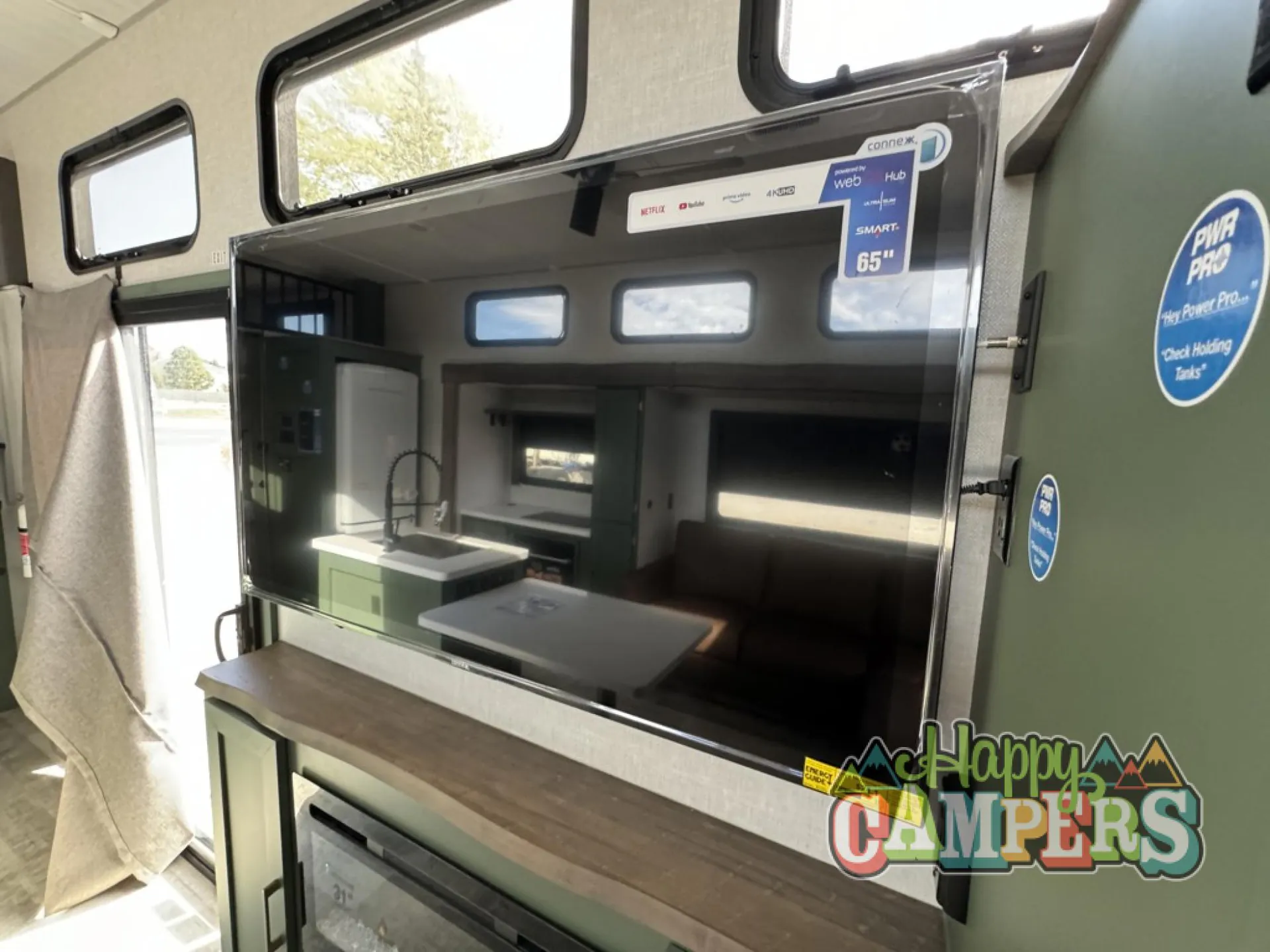 2025 Forest River IBEX RVS3 — Television reflects the lounge, kitchen sink island, dining table, refrigerator, and opposite seating area