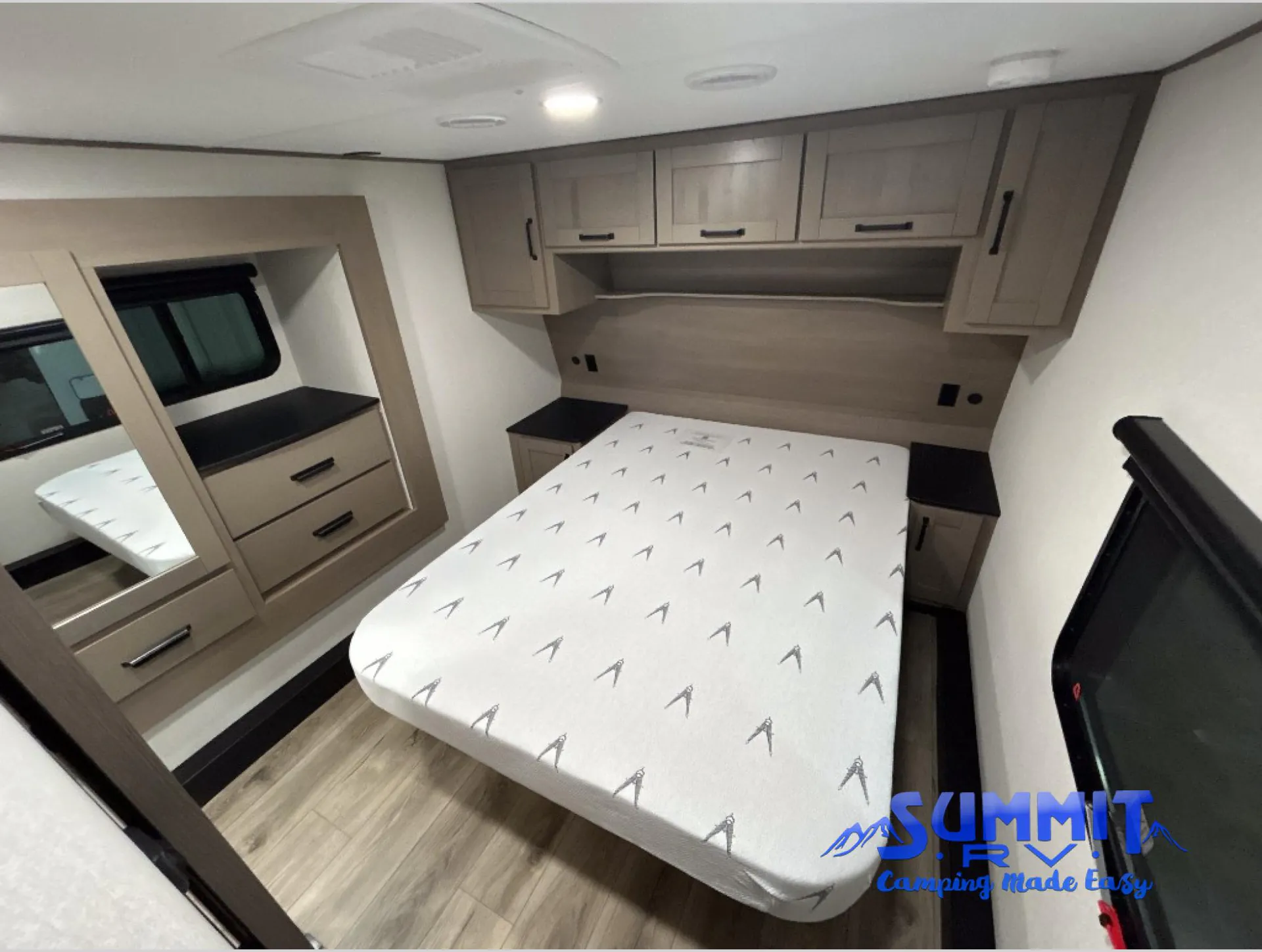 2027 Grand Design Reflection 362TBS — Main bed with nightstands, overhead cabinets, mirrored dresser, and a television in an enclosed bedroom