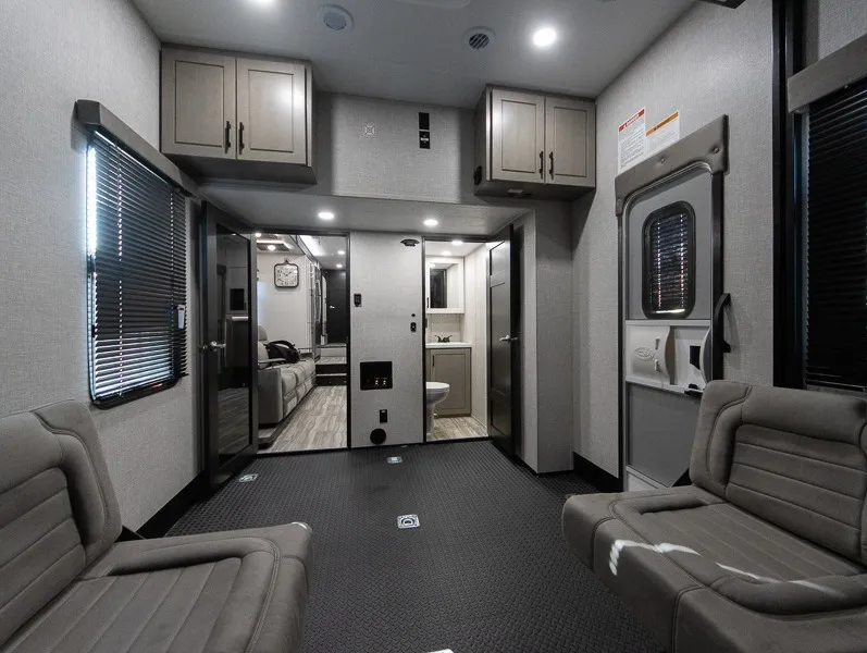 2025 Jayco Seismic Luxury Series 4113 — Garage seating and rubber cargo floor facing a hallway with an open bathroom vanity and toilet visible beyond